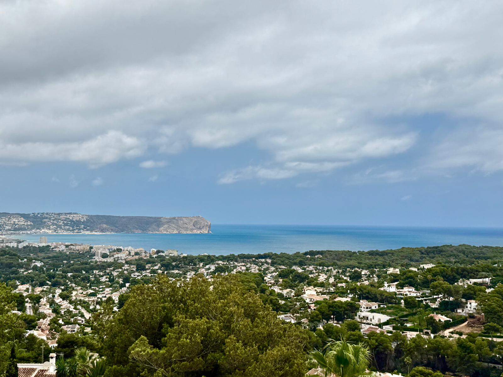 Erhöhter Panoramablick über die Bucht von Jávea und das Mittelmeer, mit Sicht auf die markante Landzunge und die bewaldete Wohngegend.