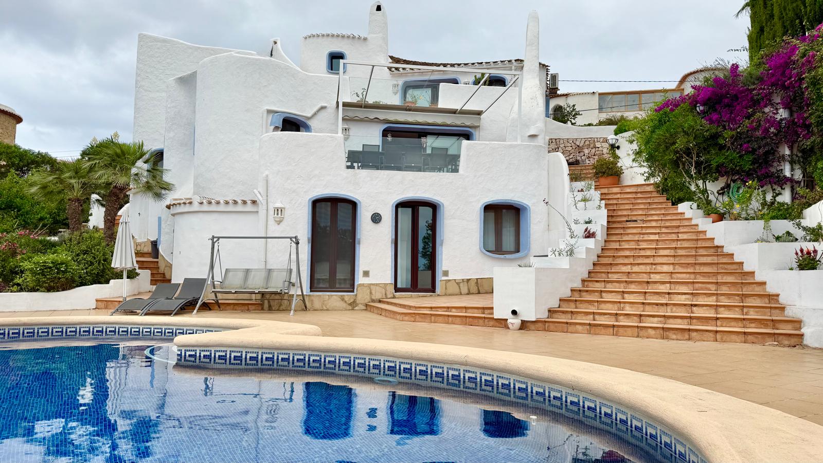 Fassade im ibizenkischen Stil mit organischen weißen Formen und terrassierten Ebenen, die über Außentreppen mit dem Poolbereich verbunden sind.