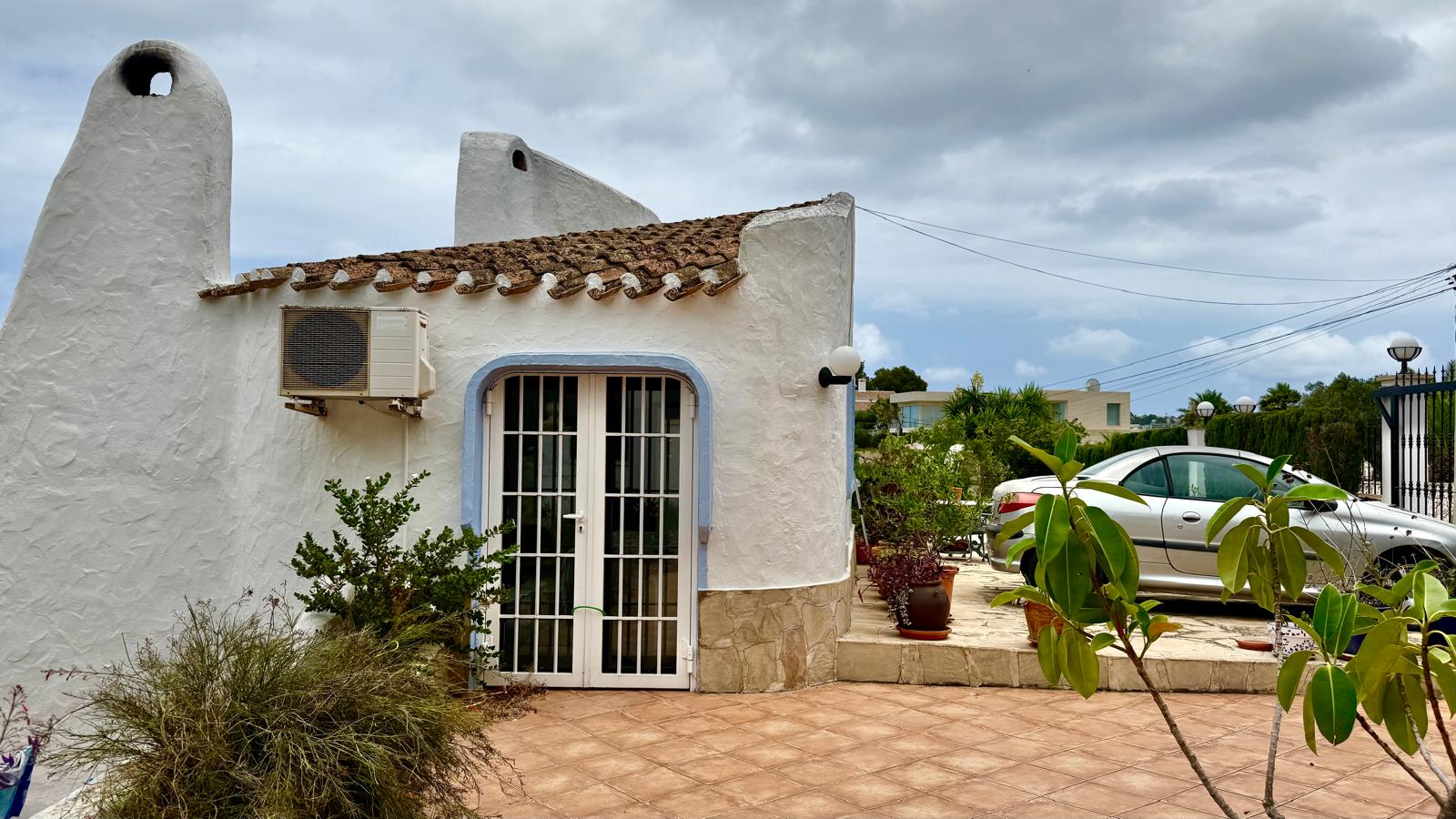 Fassade im ibizenkischen Stil mit weiß getünchten, abgerundeten Wänden und traditionellen Schornsteinen. Ebenerdiger Zugang mit Parkplatz und gefliester Terrasse.