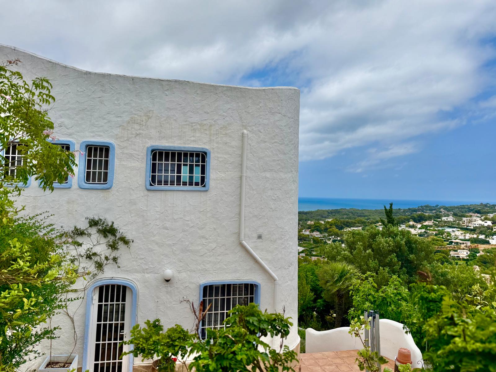 Fassade im ibizenkischen Stil mit weißen Wänden und blauen Fensterrahmen, die einen Panoramablick auf das Mittelmeer und Jávea bietet.