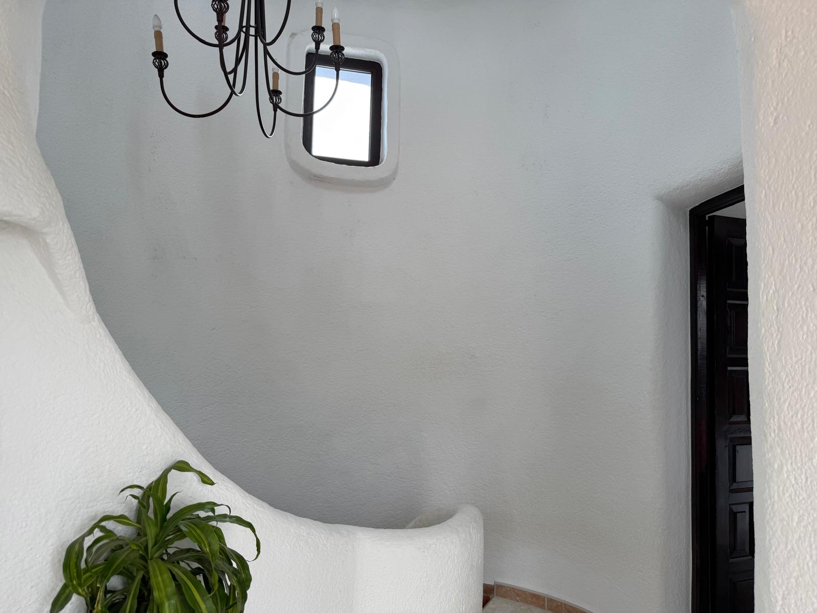 Geschwungene Innentreppe im Ibiza-Stil mit weiß verputzten Wänden, einem schmiedeeisernen Kronleuchter und einem kleinen Fenster für natürliches Licht.