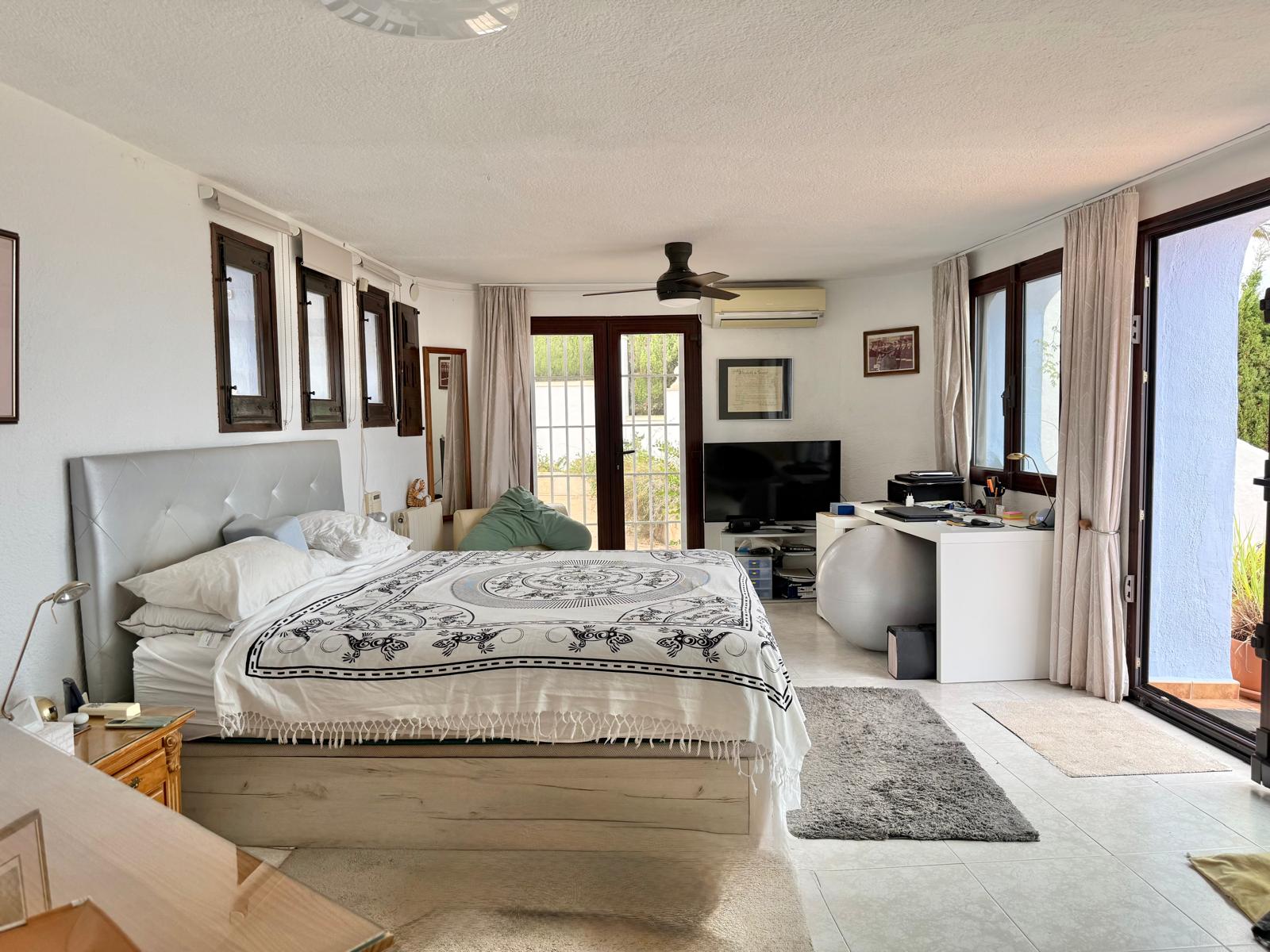 Großzügiges Hauptschlafzimmer mit Arbeitsbereich, Deckenventilator und Klimaanlage. Große Glasschiebetüren führen direkt auf die private Terrasse.