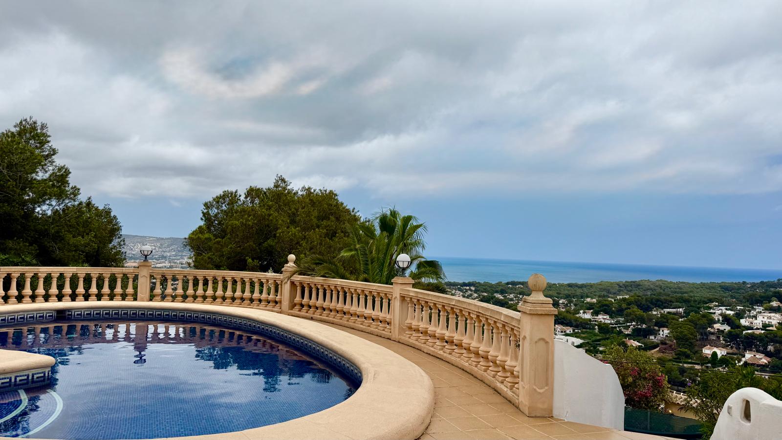 Kreisförmiger Pool mit blauen Mosaikfliesen und klassischer Steinbalustrade, der einen Panoramablick auf das Mittelmeer und die Küste von Jávea bietet.