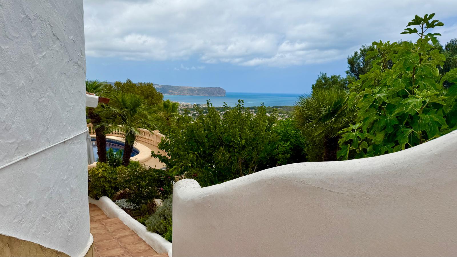 Panoramablick auf das Meer und die Bucht von Jávea von der Außentreppe aus, gesäumt von weißen geschwungenen Mauern und üppiger mediterraner Bepflanzung.