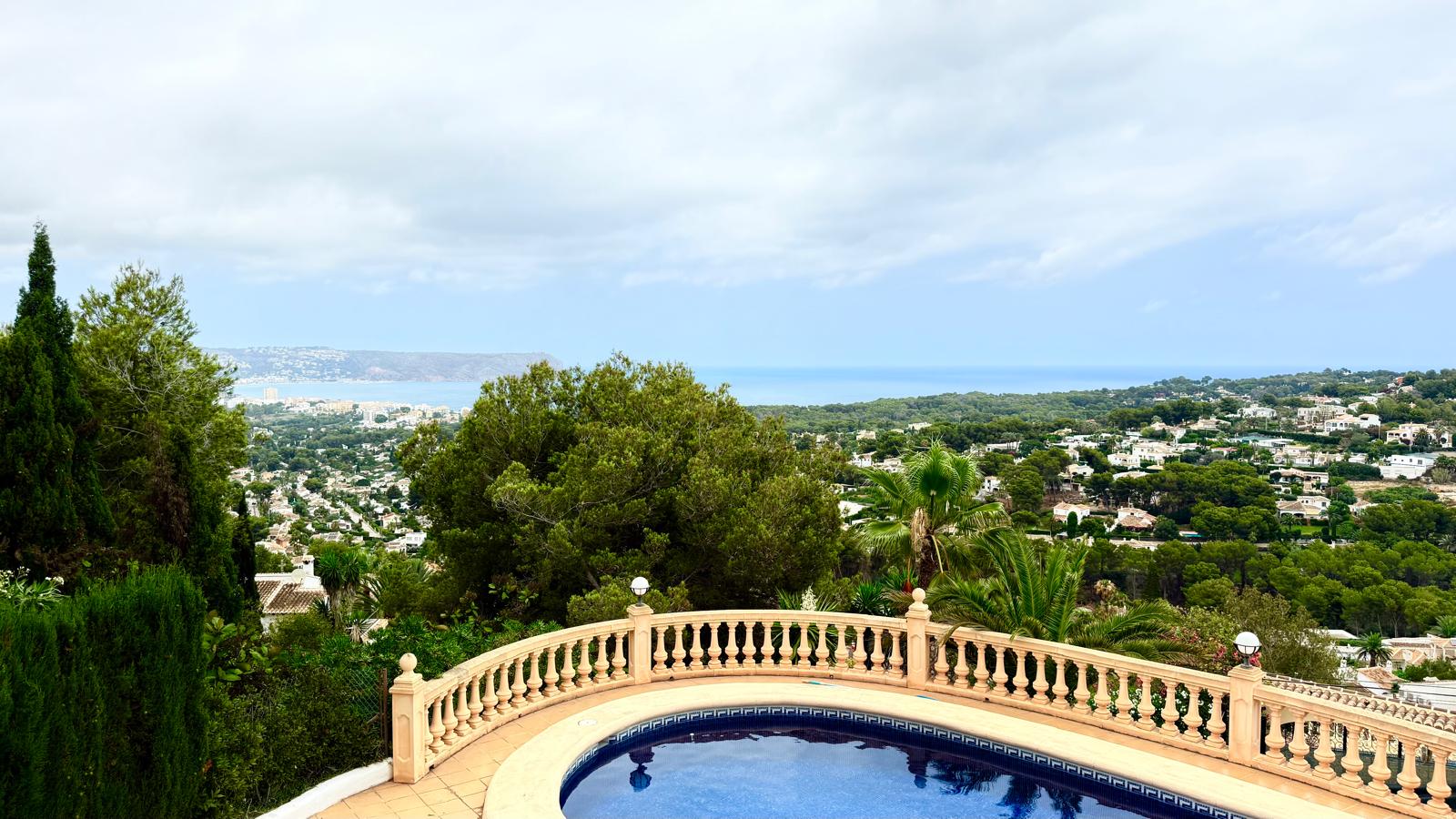 Panoramablick auf das Mittelmeer und die Bucht von Jávea von der oberen Terrasse mit klassischer Steinbalustrade über dem Poolbereich.