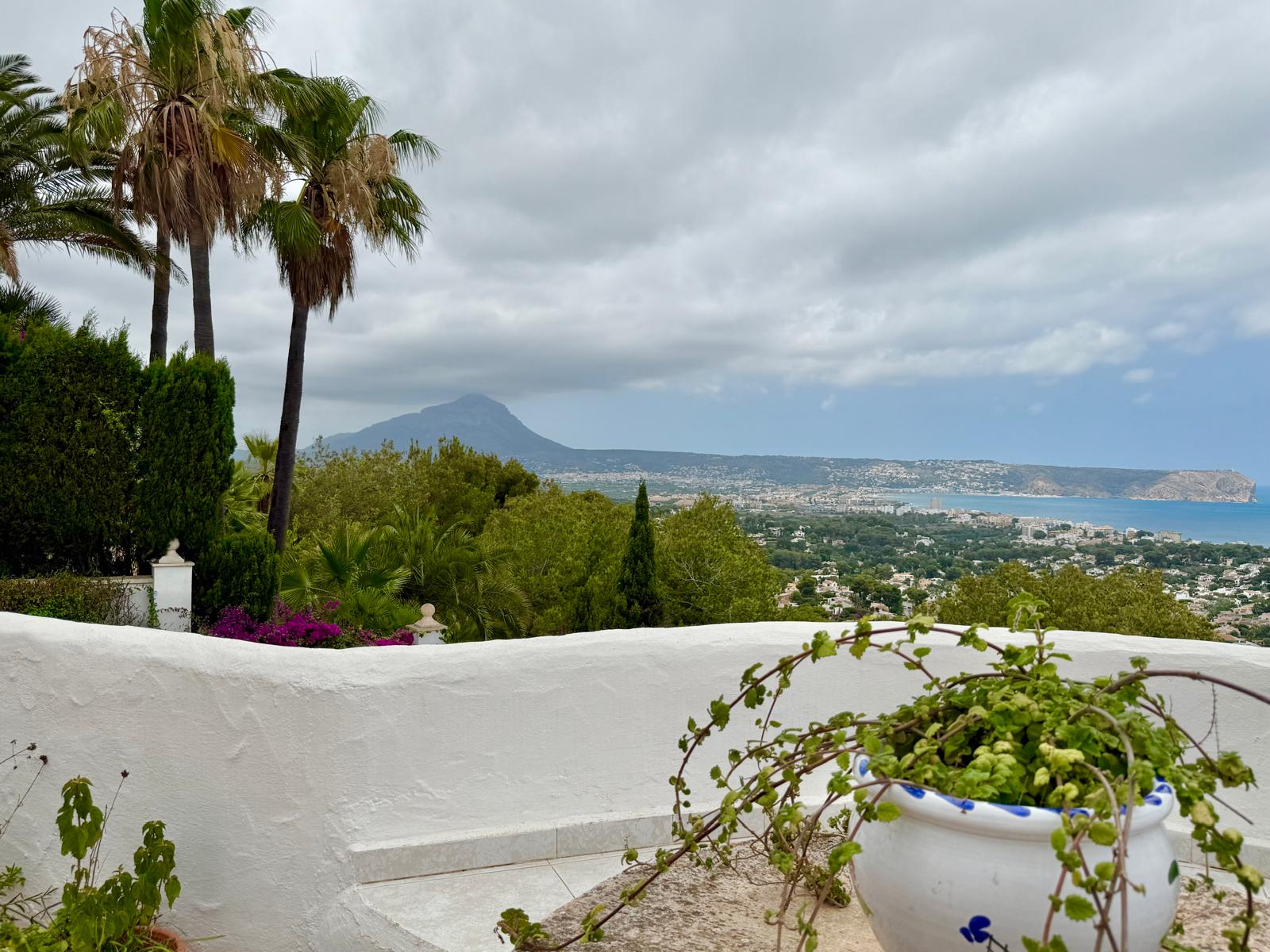 Panoramablick von der oberen Terrasse auf die Bucht von Jávea und den Berg Montgó, eingerahmt von weißen Mauern im Ibiza-Stil und mediterraner Bepflanzung.