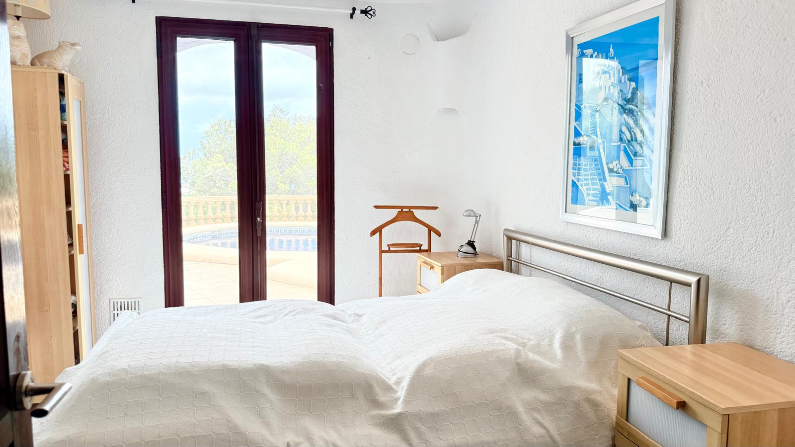 Schlafzimmer mit direktem Zugang zur Poolterrasse, strukturierten weißen Wänden, Holzmöbeln und Blick ins Freie durch Glastüren.