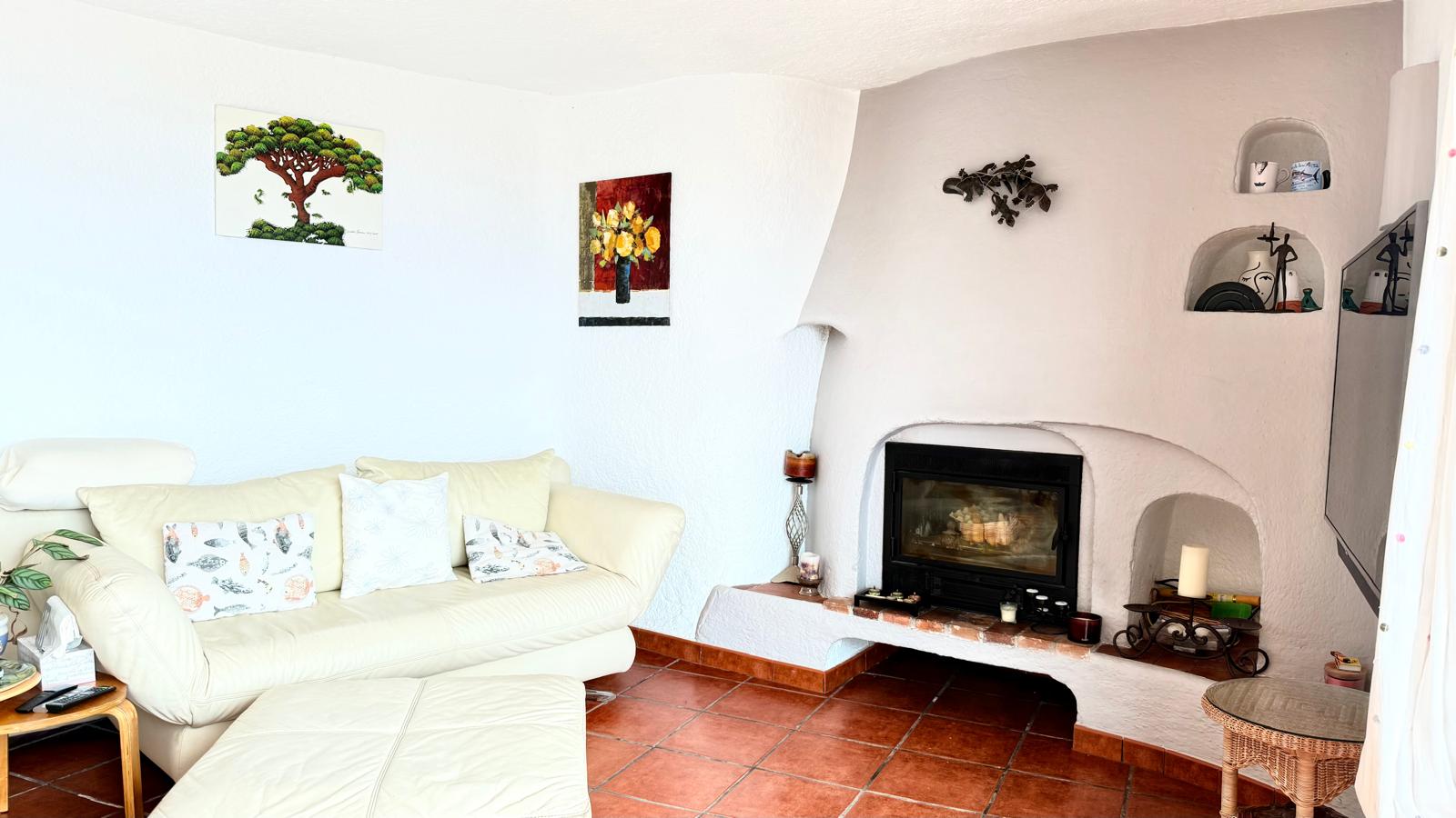 Wohnzimmer im Ibiza-Stil mit geschlossenem Kamin, dekorativen Wandnischen, traditionellen Terrakotta-Fliesen und charakteristischen weißen Strukturwänden.