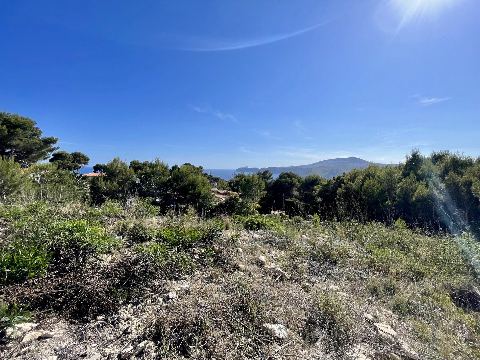 Panoramablick vom Baugrundstück auf das Mittelmeer und die Küstenlinie, eingebettet in eine natürliche Umgebung mit Pinien und Felsen.