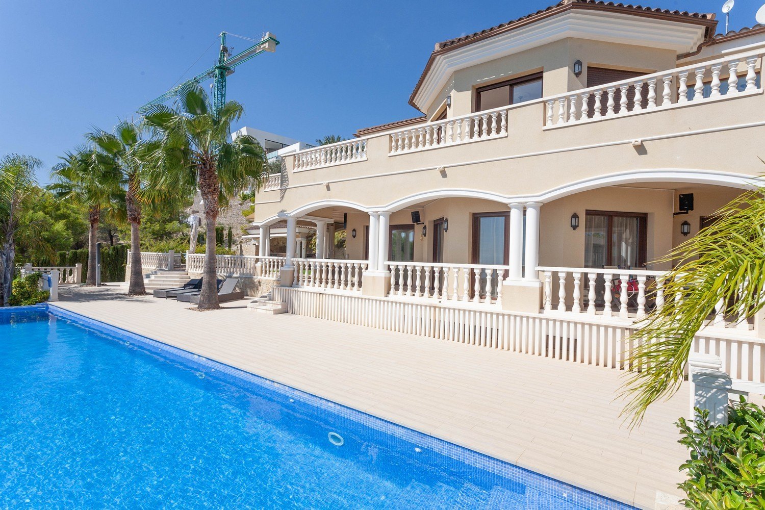 Blick auf den Pool und die Fassade der mediterranen Villa mit weißem Balustradengeländer.
