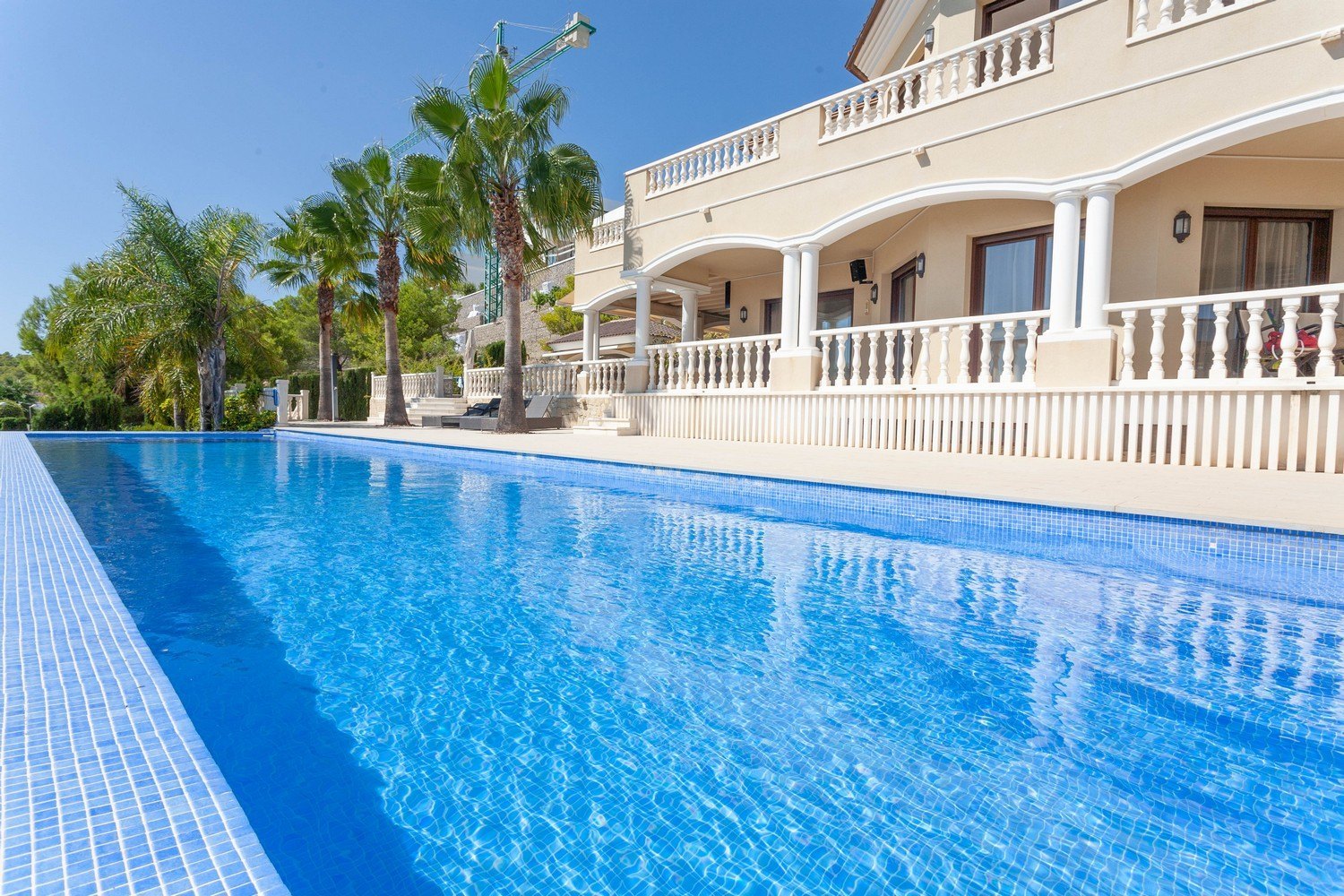 Blick auf den türkisblauen Pool mit Mosaikrand und die Fassade der Villa im mediterranen Stil.