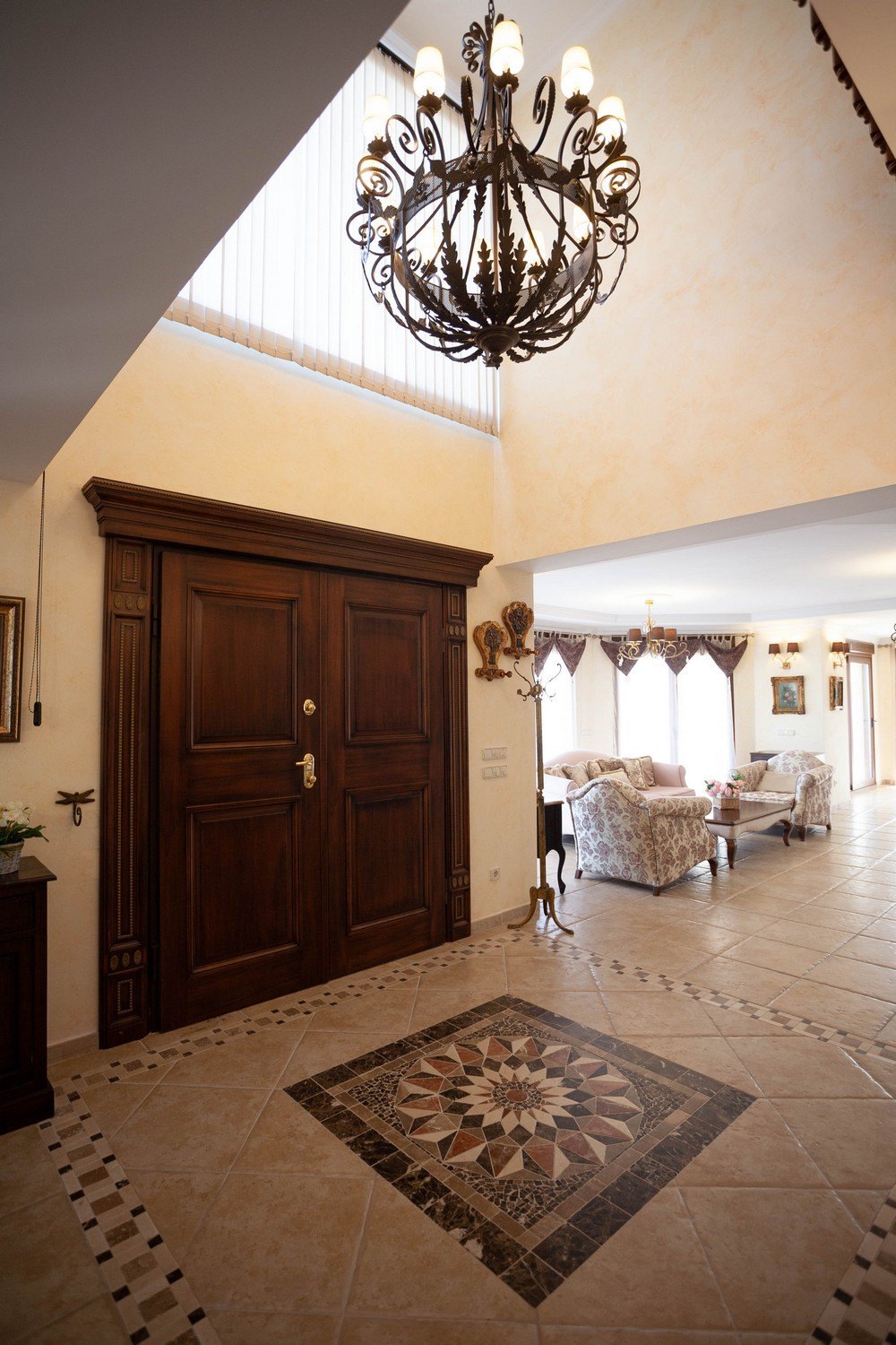 Foyer mit dunklen Holztüren und kunstvollem Kronleuchter. Fliesenboden mit geometrischem Muster.