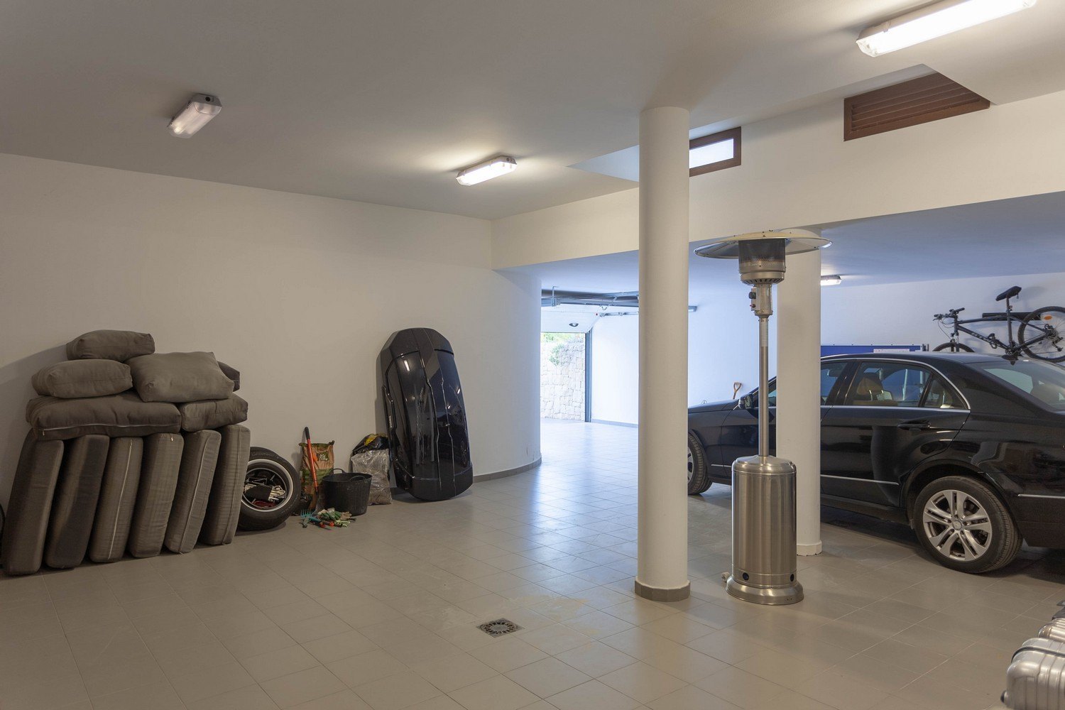 Geräumige Garage mit Fliesenboden, schwarzem Auto und diversen gelagerten Zubehör.