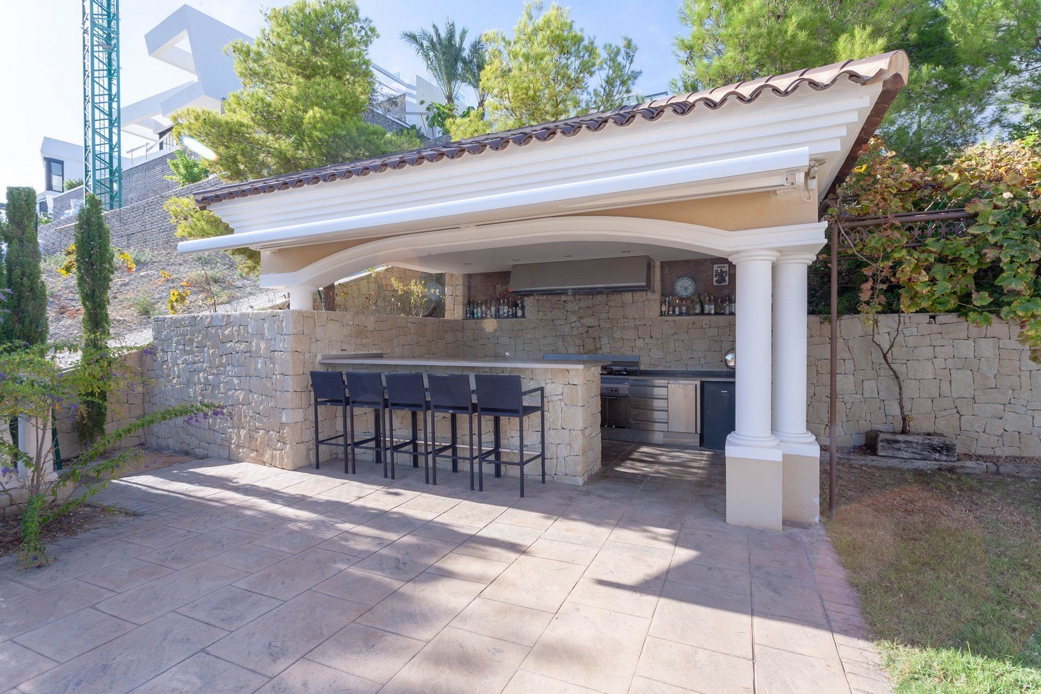 Grillplatz im Freien mit Bar und Hockern in Villa in Benissa. Steinverkleidung und Arbeitsplatte aus Edelstahl.