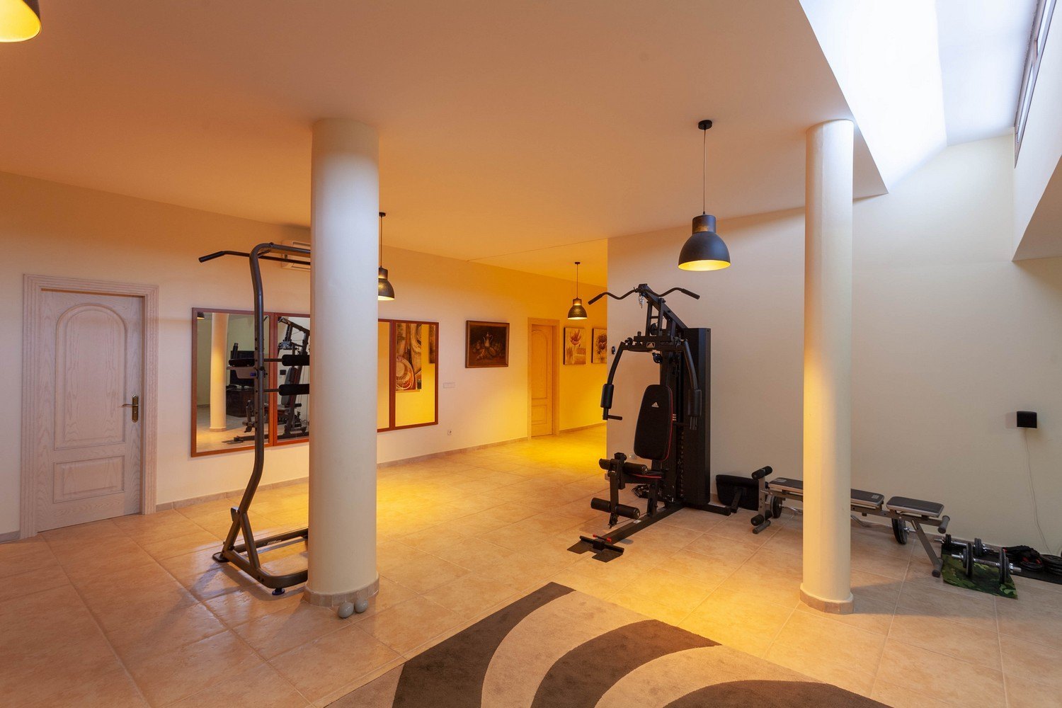 Heller Fitnessraum mit Fliesenboden, ausgestattet mit Trainingsgeräten und Oberlicht.