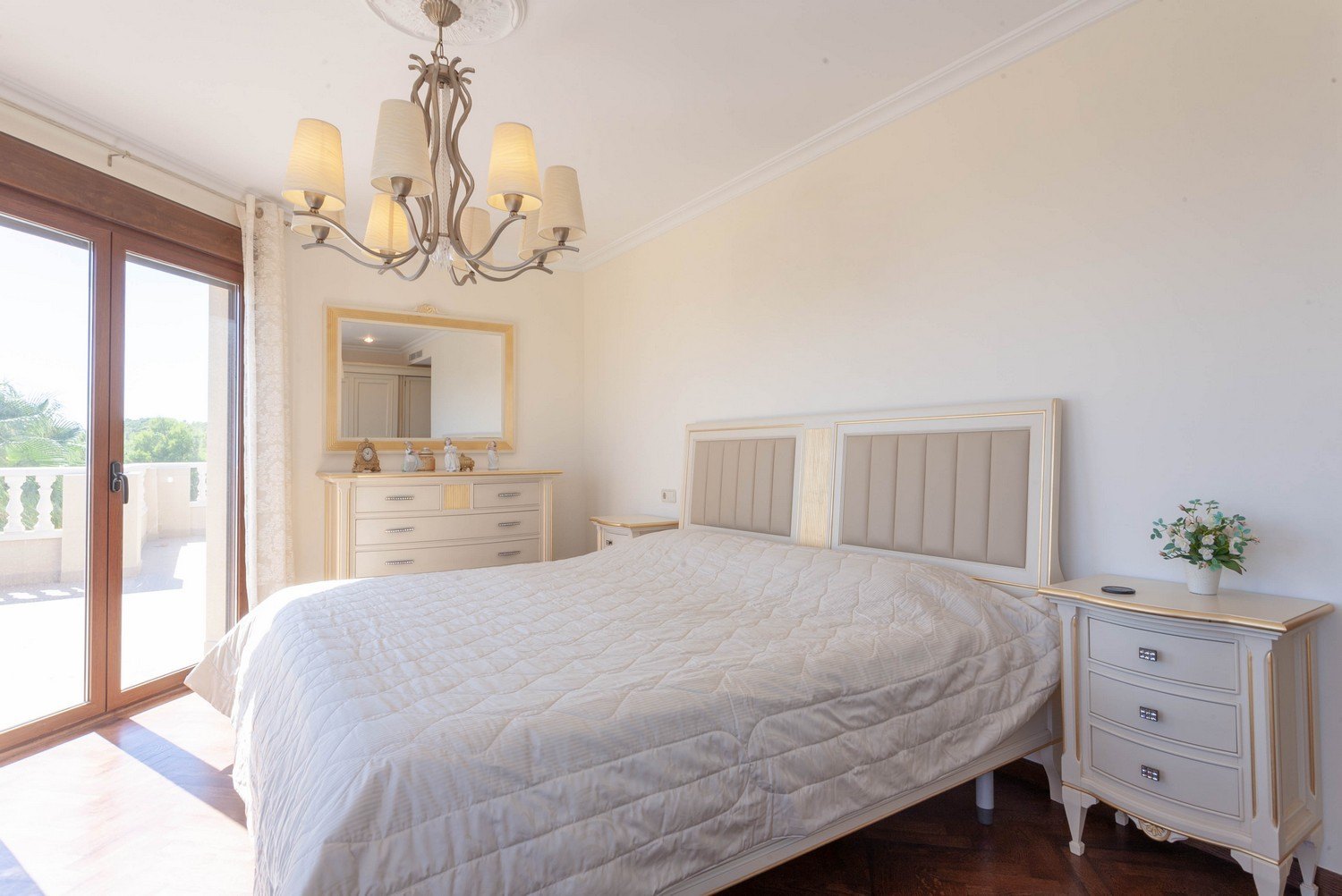 Helles Schlafzimmer mit Doppelbett, Nachttischen und klassischer Kommode mit goldgerahmtem Spiegel.