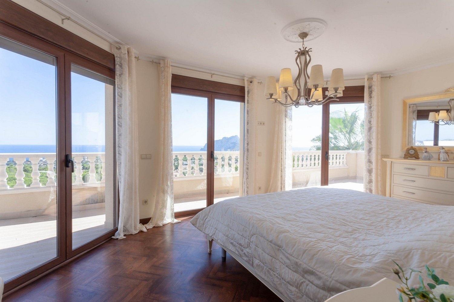 Helles Schlafzimmer mit Meerblick, Balustradenbalkon und Fischgrätenparkett.