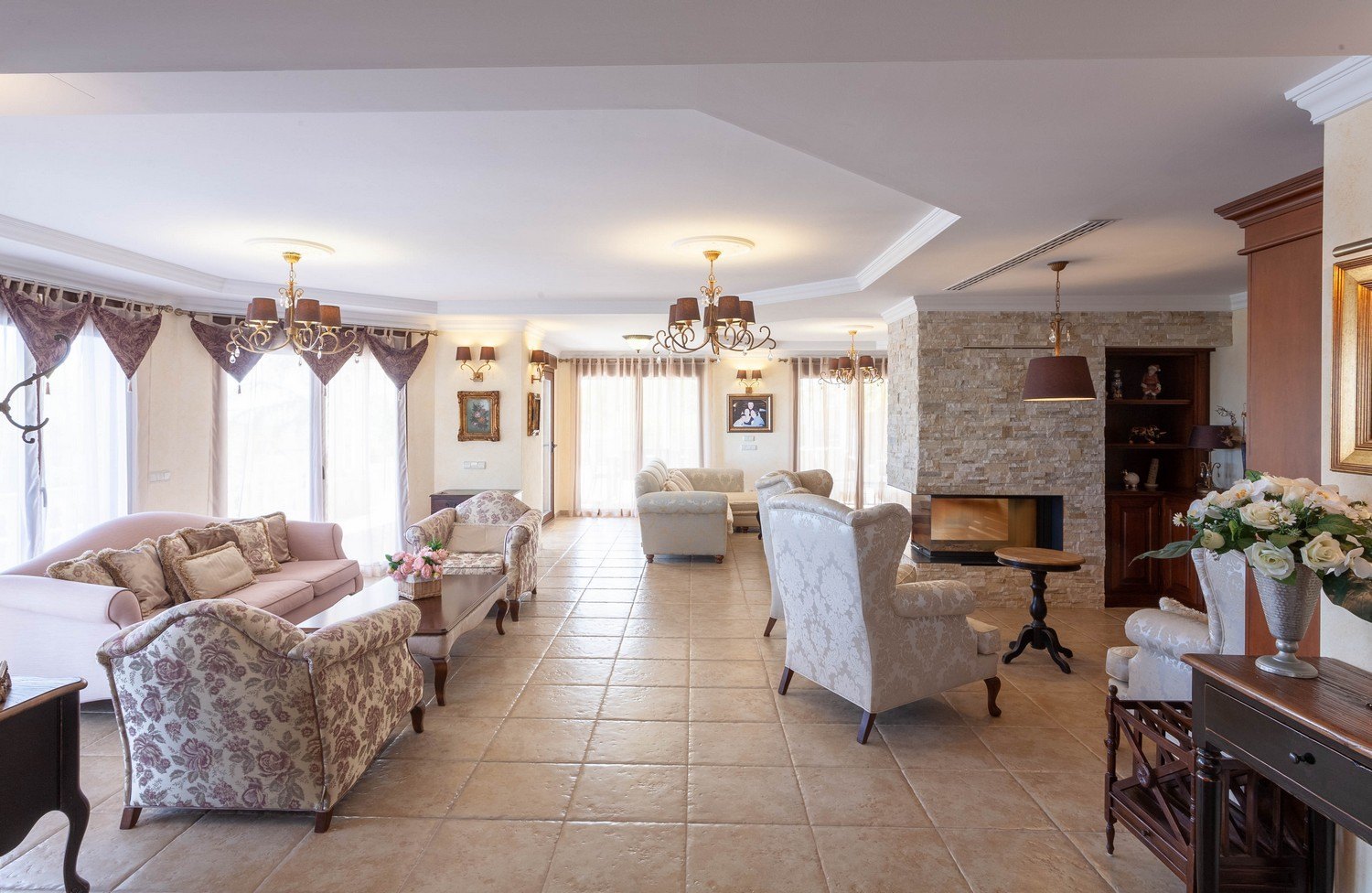 Helles Wohnzimmer mit Steinkamin, gemusterten Sofas und verzierten Fenstergardinen.