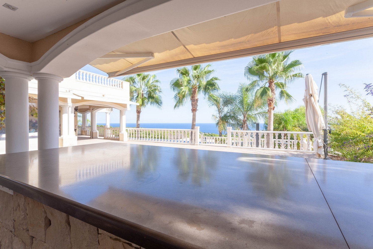 Überdachte Terrasse mit Steinbar und Blick auf das Meer und Palmen in Raco de Galeno, Benissa.