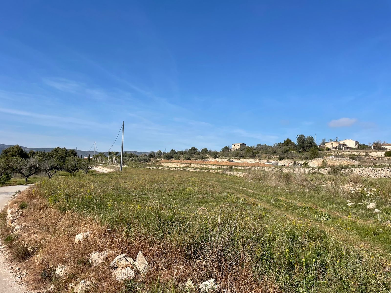 Blick auf rustikales Gelände in Jávea mit erhöhten Bauten und klarem blauem Himmel.