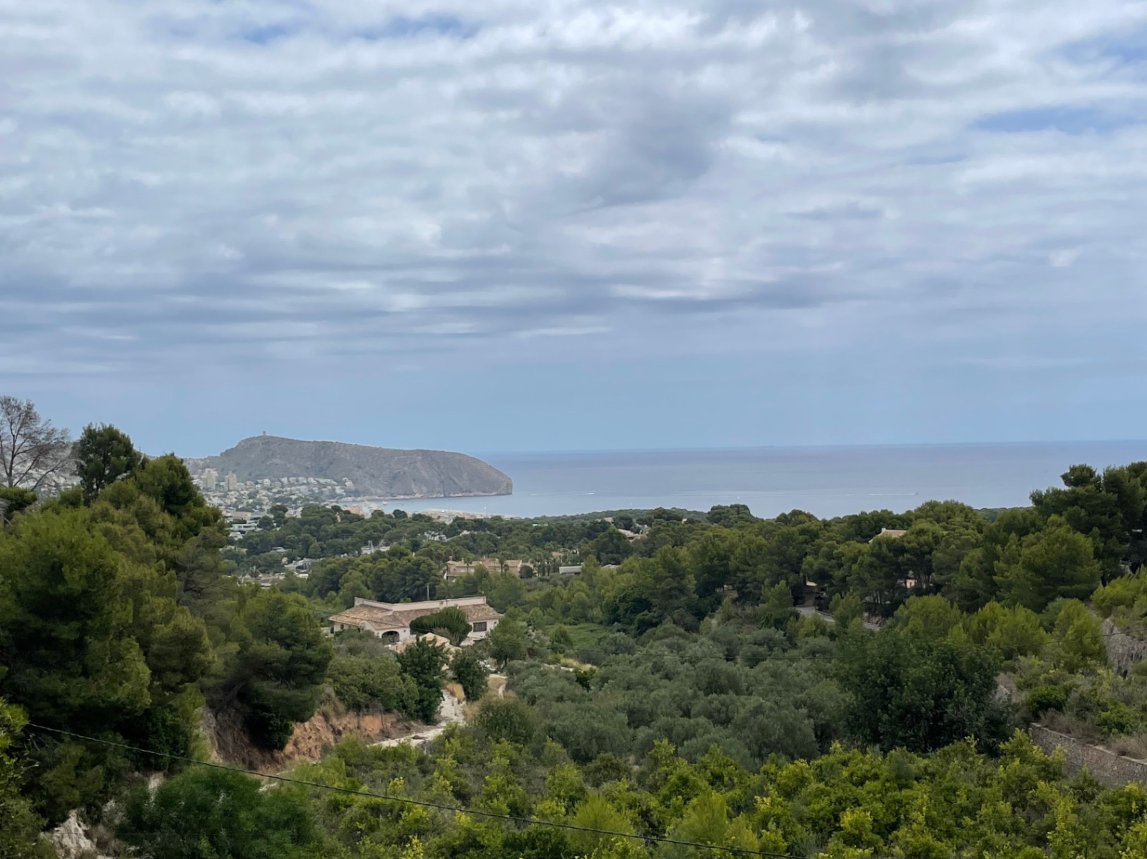 Panoramablick auf das Mittelmeer und das Cap d'Or von der Anhöhe in Benimeit, umgeben von üppiger mediterraner Vegetation und Pinien.
