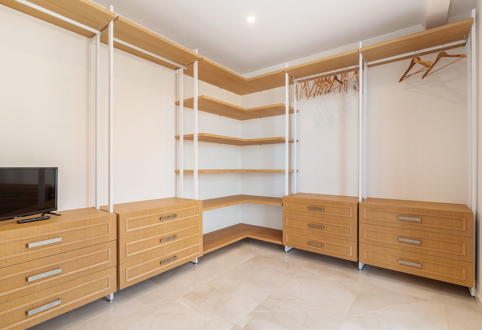 Begehbarer Kleiderschrank mit hellen Holzregalen, integrierten Schubladenelementen und Feinsteinzeugboden in Marmoroptik mit Deckenstrahlern.