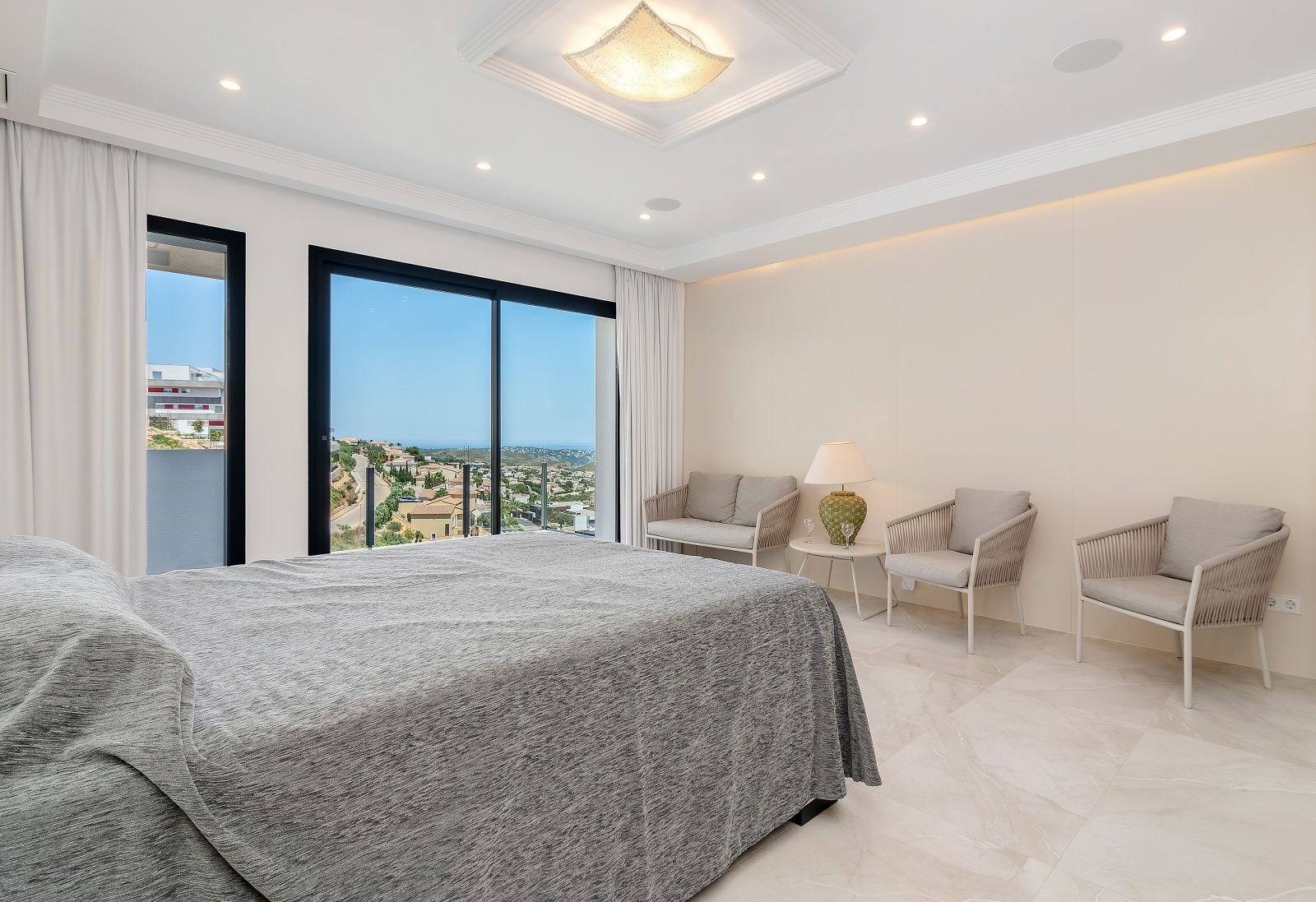 Hauptschlafzimmer mit Marmorboden, integriertem Sitzbereich und großen Glasschiebetüren mit Panoramablick auf das Meer und die Küste.