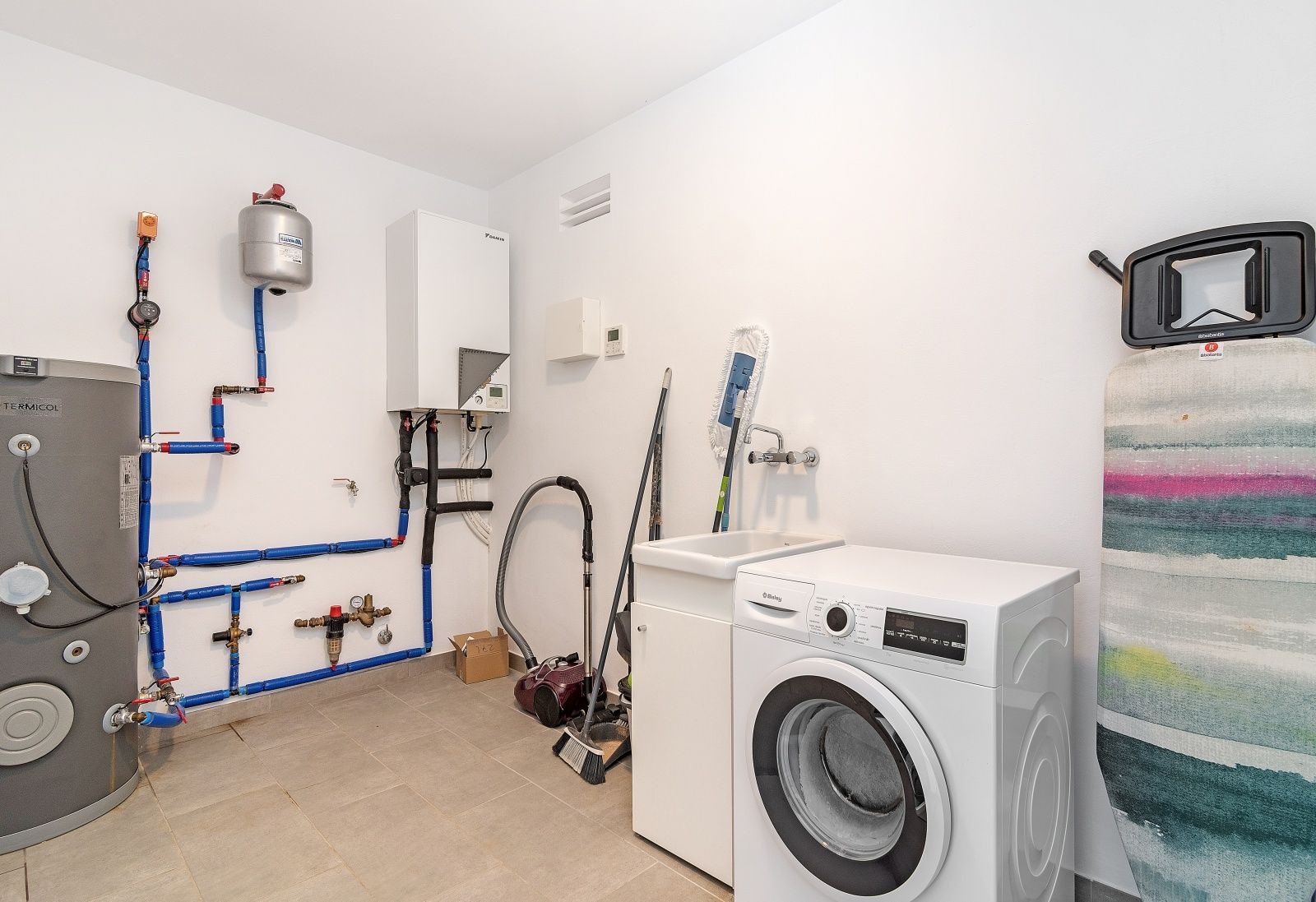 Hauswirtschaftsraum und Technikraum mit Waschmaschine, Spülbecken, Daikin-Wärmepumpe und Warmwasserspeicher.