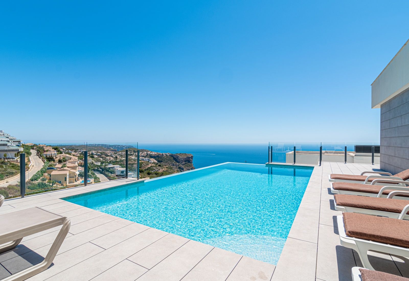 Infinity-Pool mit Panoramablick auf das Mittelmeer, umgeben von einer großzügigen Fliesenterrasse mit Sonnenliegen und Glasgeländern.