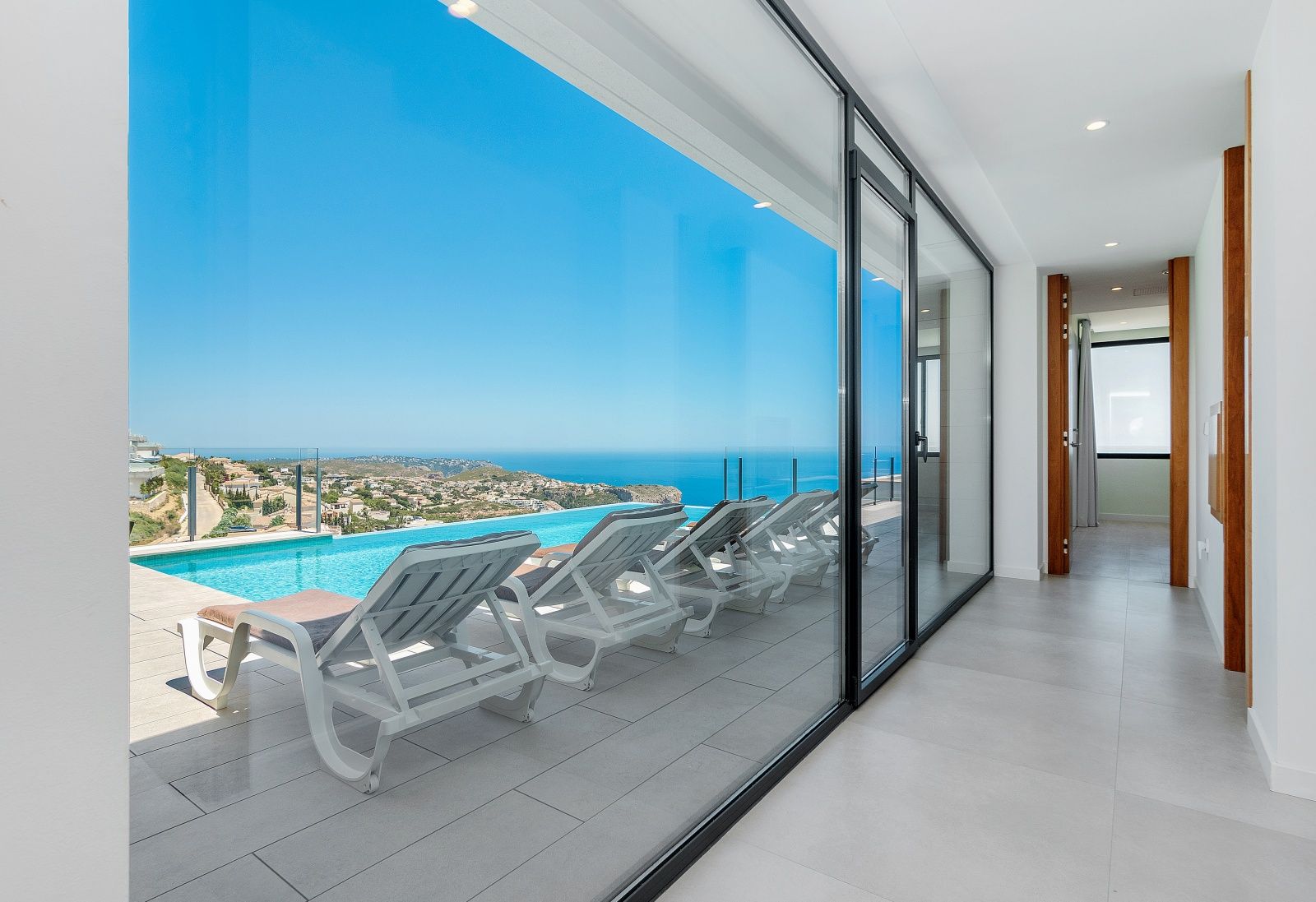 Innenflur mit bodentiefen Glasfronten, die einen Panoramablick auf das Meer und direkten Zugang zur Terrasse mit Infinity-Pool bieten.