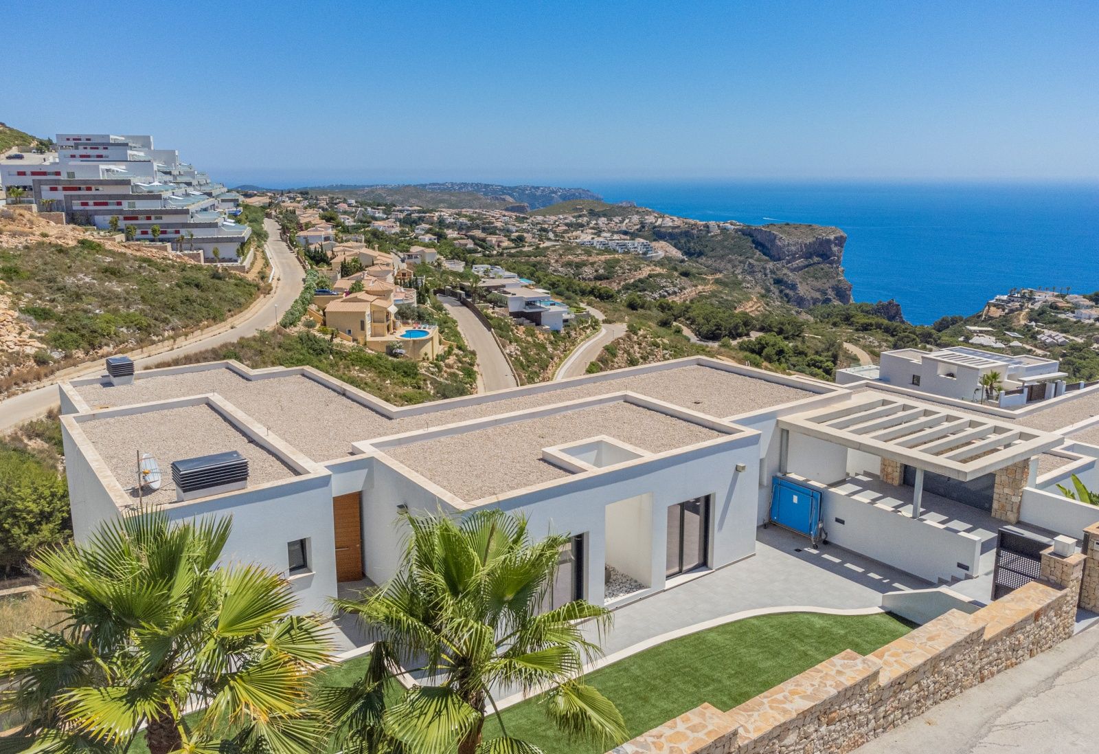 Luftaufnahme der modernen Villa in Cumbre del Sol mit weißer Architektur, Kiesflachdächern und Panoramablick auf das Mittelmeer und die markante Steilküste.