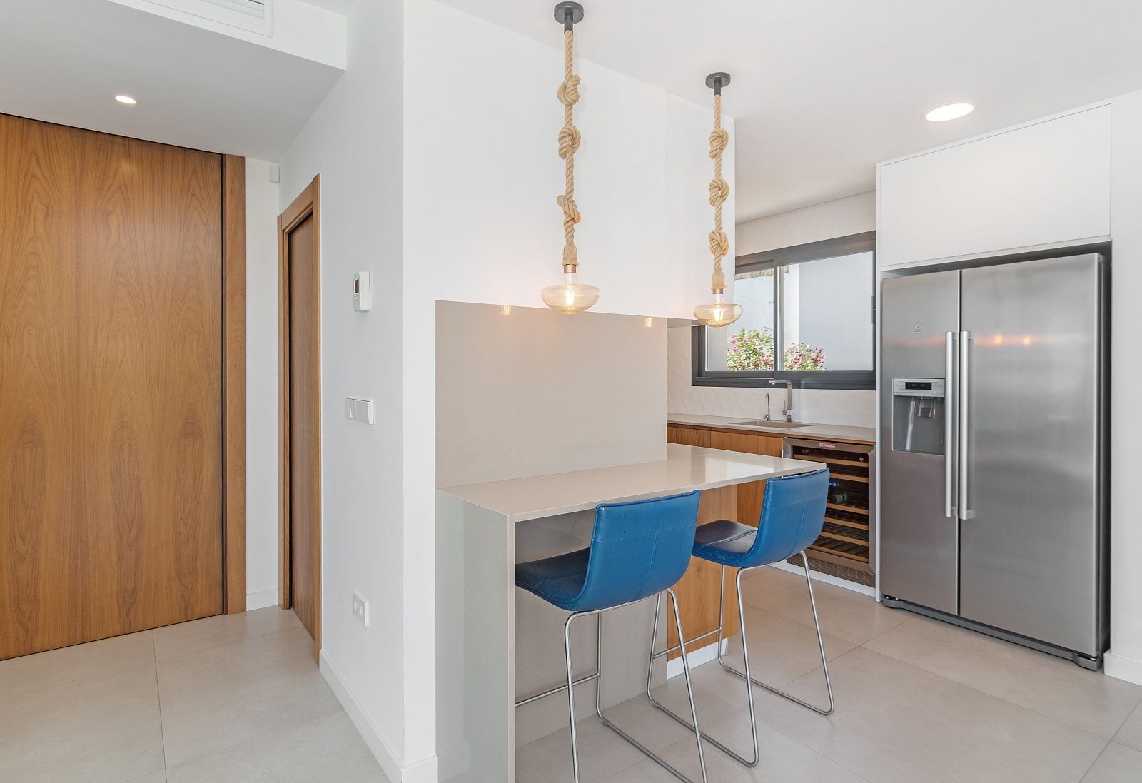 Moderne Küche mit grauer Frühstücksbar, blauen Hockern und Seil-Pendelleuchten. Ausgestattet mit einem amerikanischen Edelstahlkühlschrank und Weinkühlschrank.