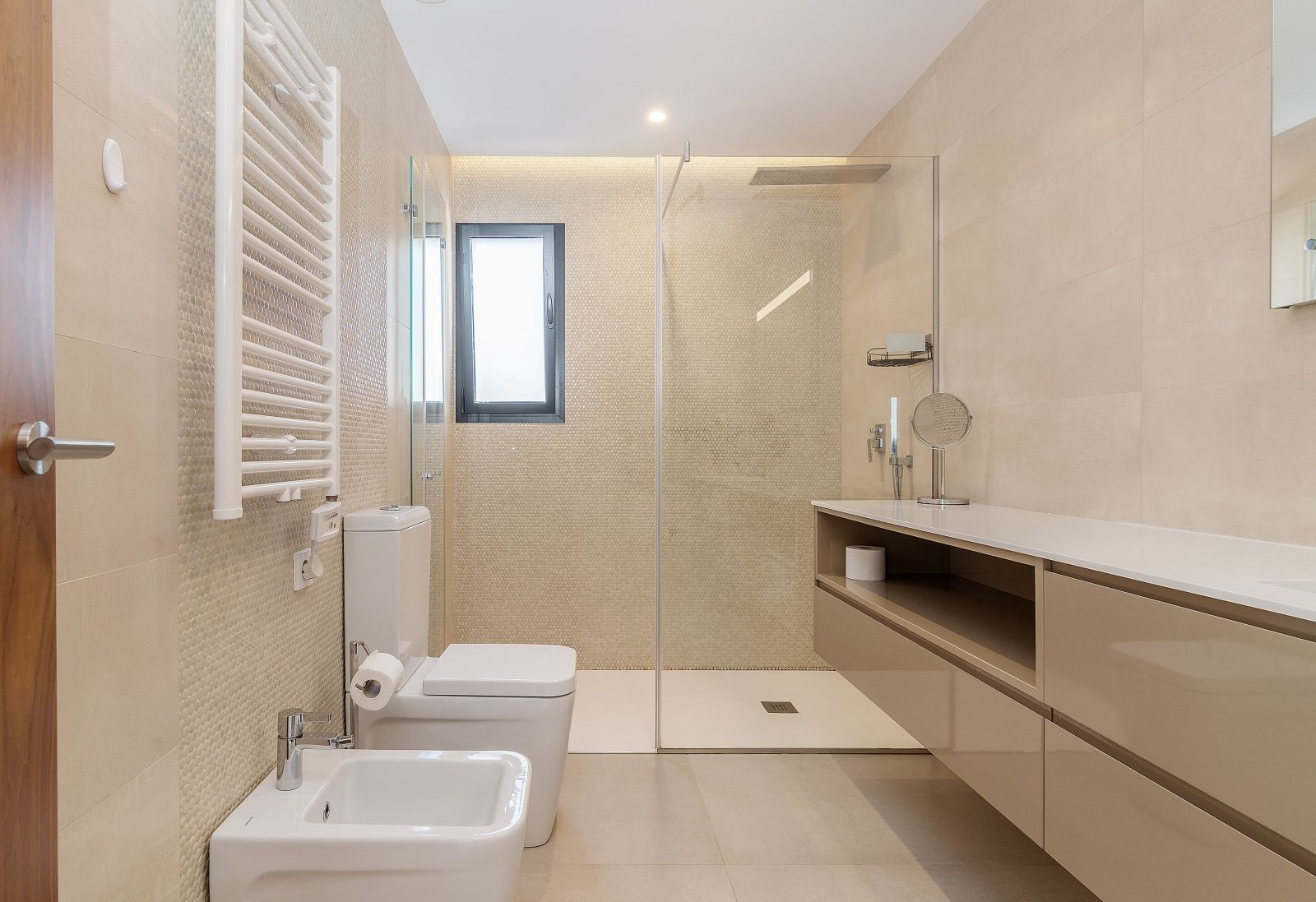 Modernes Badezimmer mit begehbarer Dusche, Glastrennwand, wandhängendem Waschtisch, Bidet und weißem Handtuchheizkörper in hellen Beigetönen.