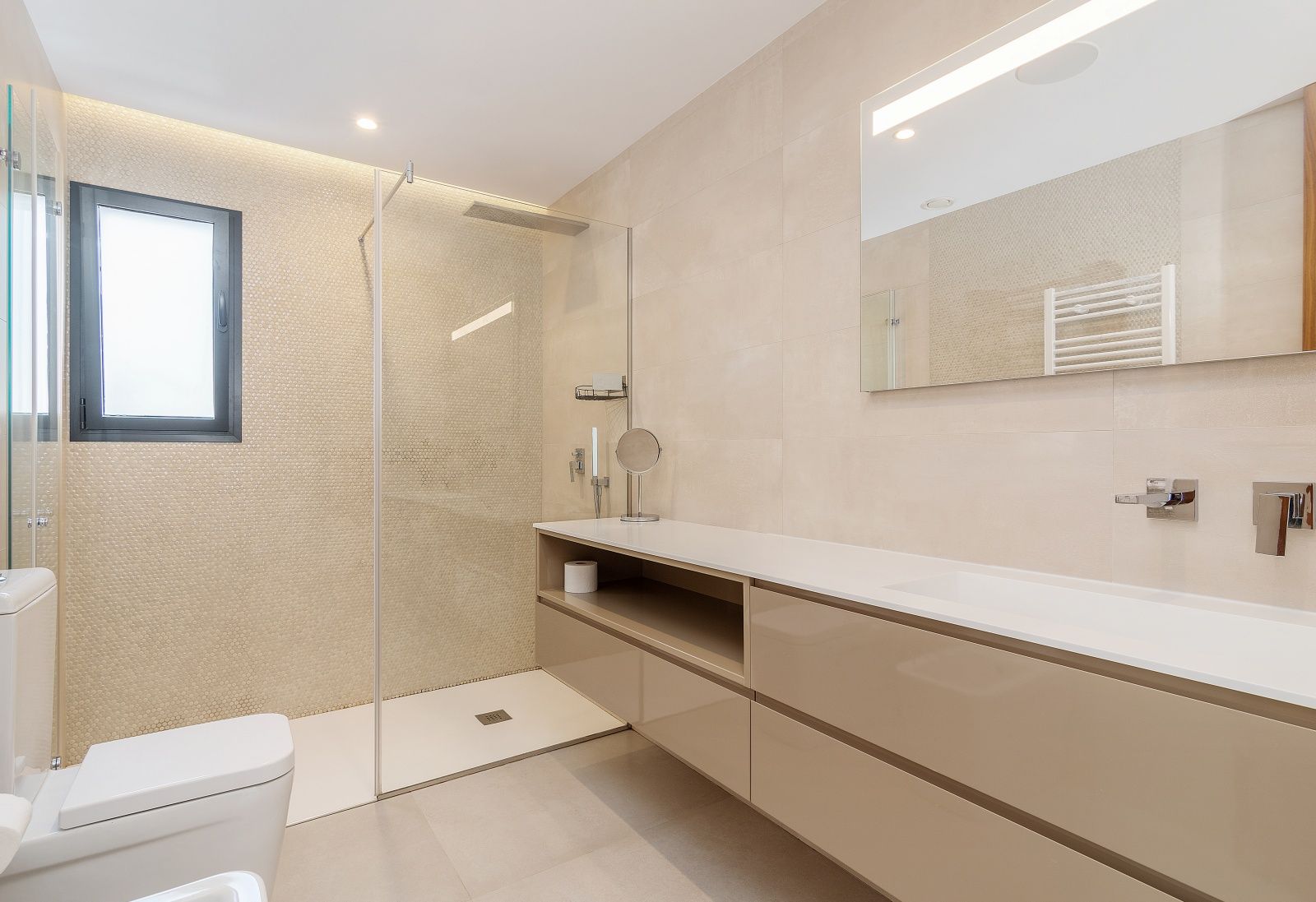 Modernes Badezimmer mit begehbarer Dusche, Glaswand und Mosaikfliesen. Ausgestattet mit einem schwebenden beigen Waschtisch, integriertem Waschbecken und LED-Spiegel.
