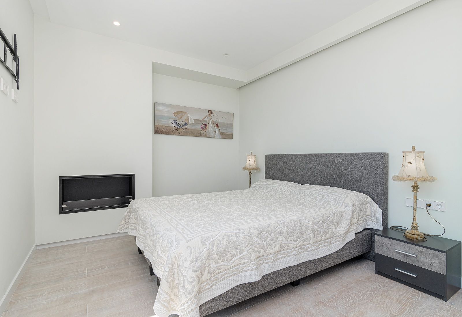 Modernes Schlafzimmer mit wandintegriertem Kamin, Feinsteinzeug in Holzoptik und grau gepolstertem Bettkopfteil.