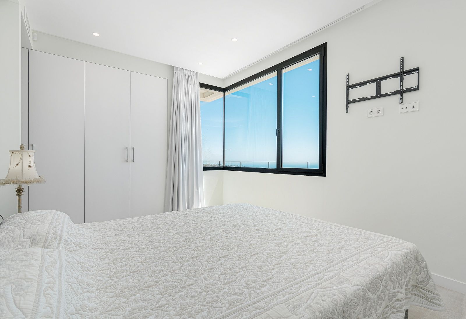 Modernes Schlafzimmer mit weißen Einbauschränken, Eckfenster mit schwarzen Rahmen und Panoramablick auf das Mittelmeer.