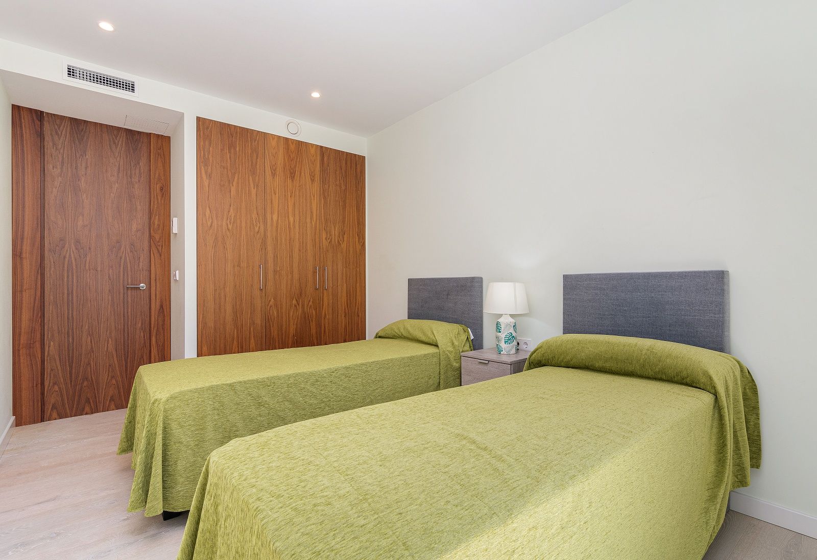 Modernes Schlafzimmer mit zwei Einzelbetten, Einbauschränken aus Naturholz, Kanalklimaanlage und dezenter Deckenbeleuchtung.