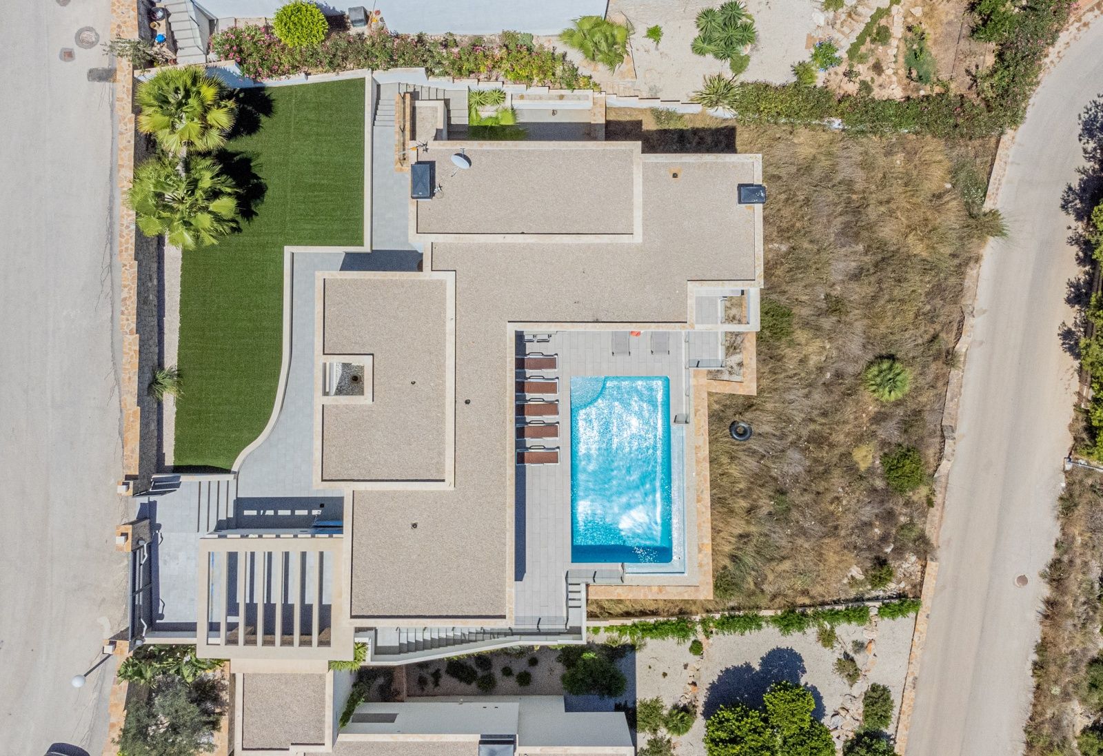 Zenithale Luftaufnahme der modernen Villa mit rechteckigem Pool, Sonnenterrasse mit Liegen und pflegeleichtem Garten mit Kunstrasen.