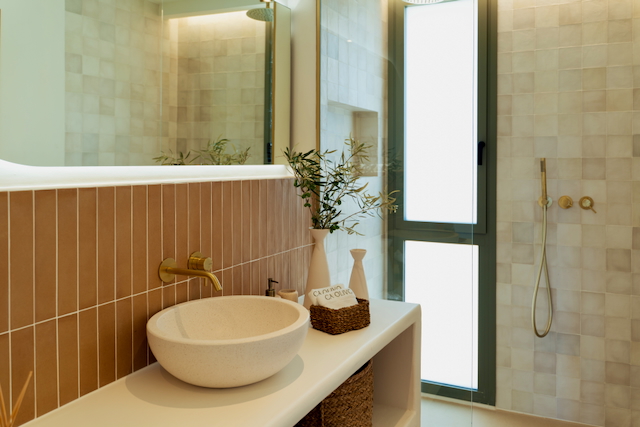 Modernes Badezimmer mit Aufsatzwaschbecken, gebürsteten Goldarmaturen und vertikalen Fliesen. Die begehbare Dusche verfügt über eine Glastrennwand und Tageslicht.