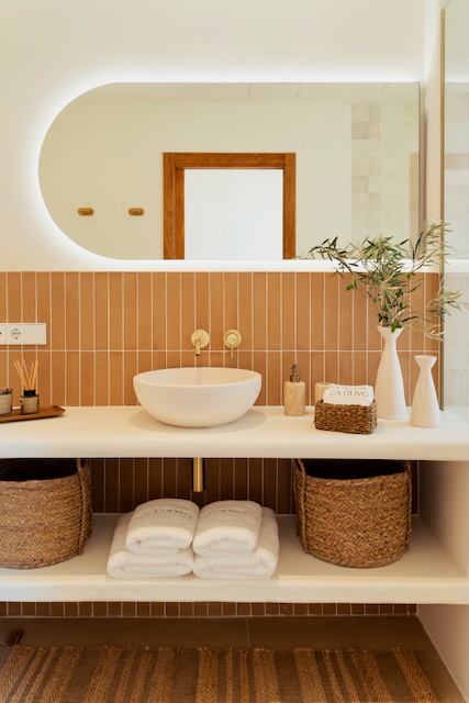 Modernes Badezimmer mit Aufsatzwaschbecken, Unterputz-Armaturen aus Messing und vertikalen Terrakotta-Fliesen. Ein ovaler, hinterleuchteter Spiegel ergänzt das offene Regalsystem.