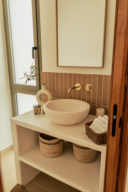 Modernes Badezimmer mit Stein-Aufsatzwaschbecken, goldener Unterputzarmatur und vertikalen terracottafarbenen Fliesen. Offener Waschtisch mit geflochtenen Aufbewahrungskörben.