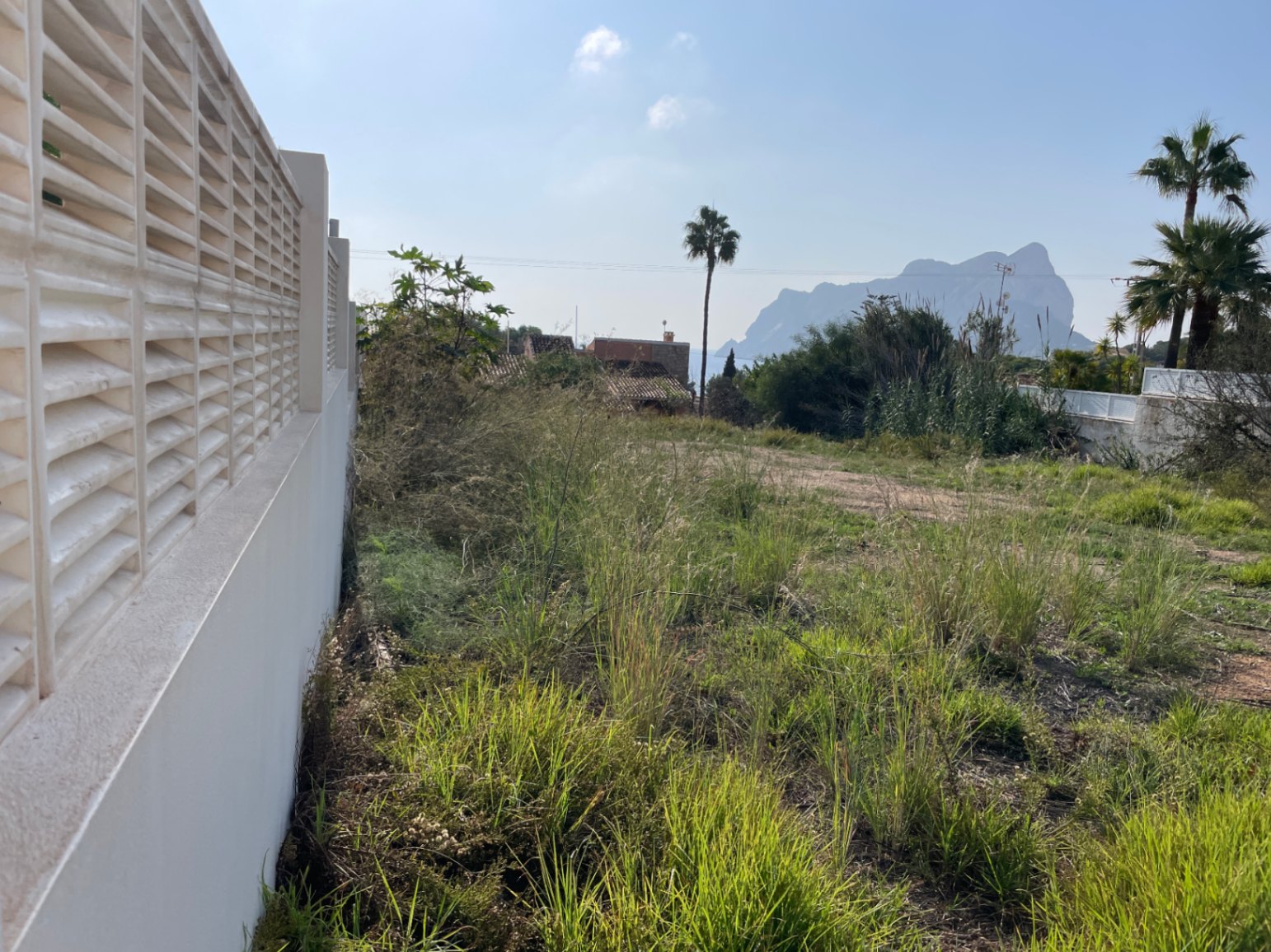 Baugrundstück von 856 m² in Bassetes, Calpe, mit weißer Begrenzungsmauer und direktem Blick auf den Peñón de Ifach in der Ferne.