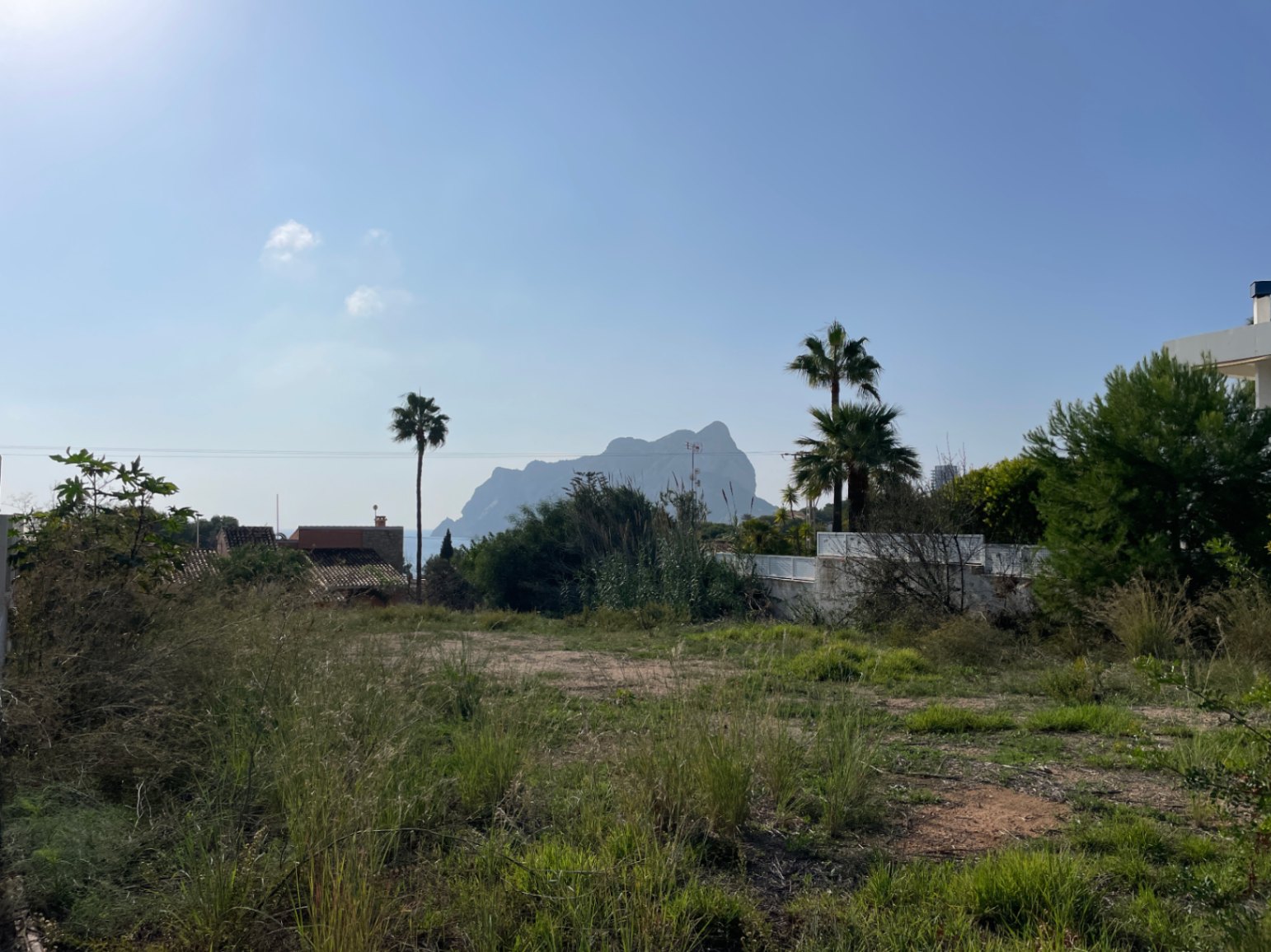 Ebenes Baugrundstück in Bassetes mit freiem Blick auf den Peñón de Ifach, umgeben von typisch mediterraner Vegetation und Palmen.