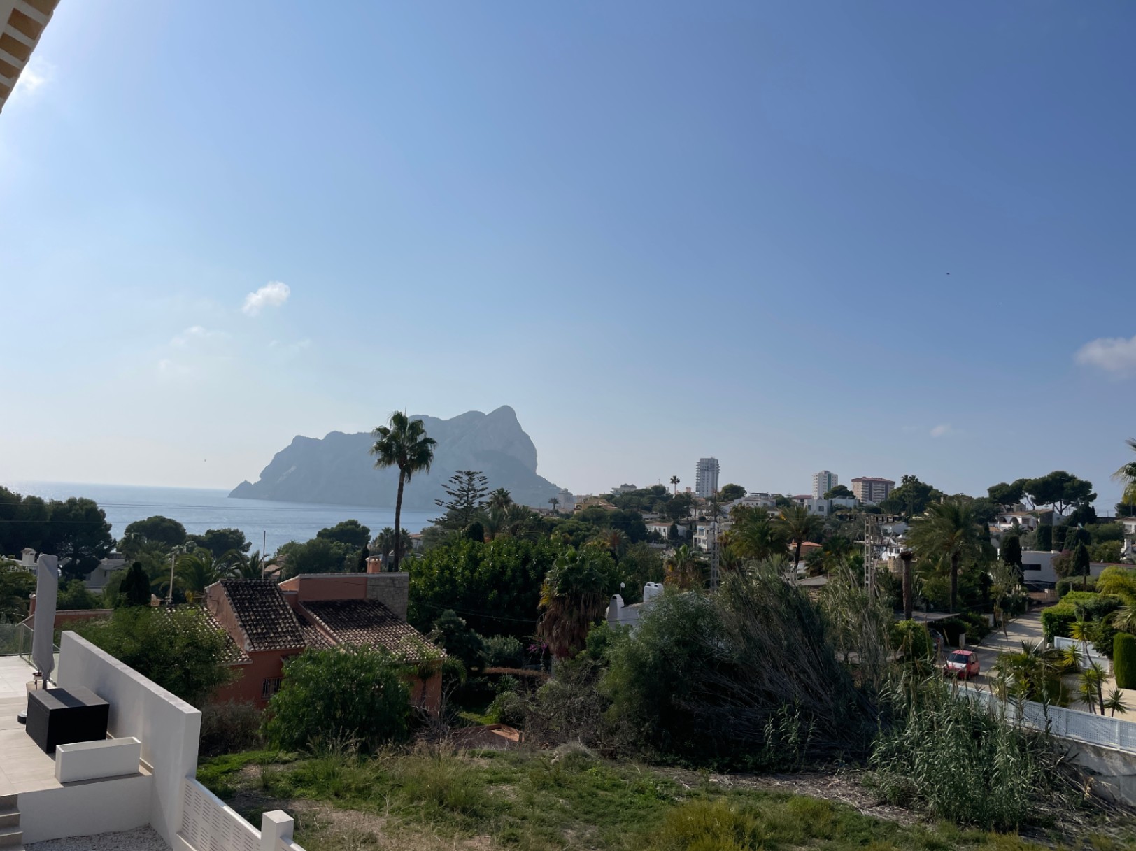 Panoramablick auf den Peñon de Ifach und das Mittelmeer vom erhöhten Grundstück in Bassetes, Calpe, umgeben von mediterraner Vegetation und Wohnbebauung.