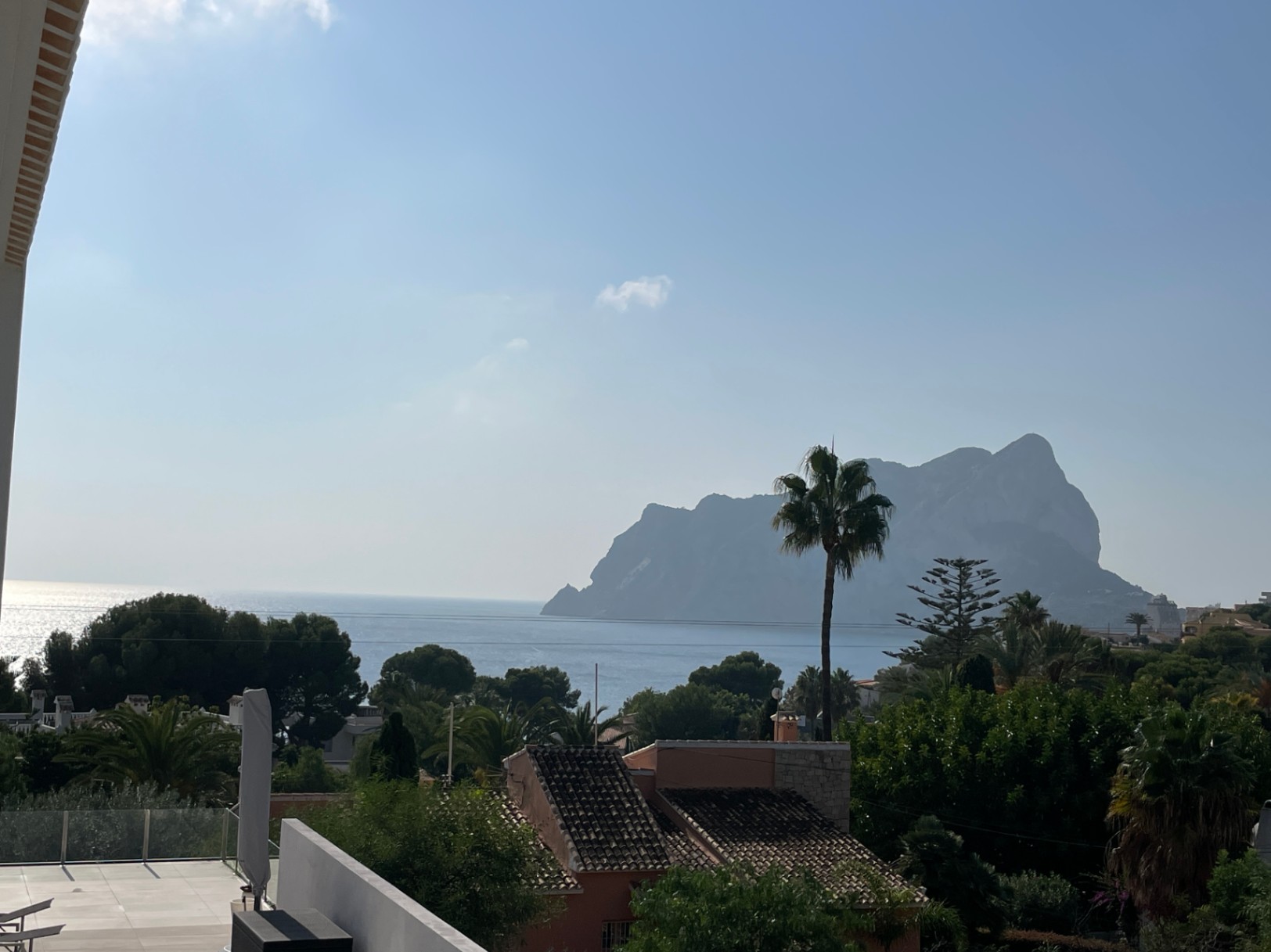 Panoramablick auf den Peñón de Ifach und das Mittelmeer von einer erhöhten Terrasse mit Glasgeländer und mediterraner Vegetation.