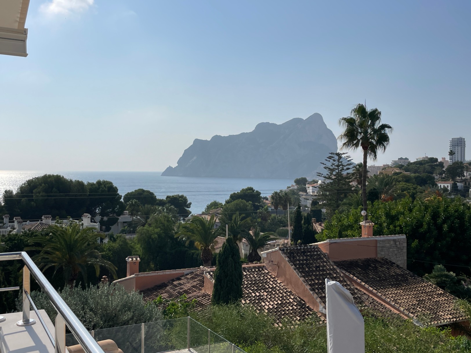 Panoramablick von der Terrasse auf den Peñón de Ifach und das Mittelmeer, eingebettet in mediterrane Vegetation und traditionelle Ziegeldächer.