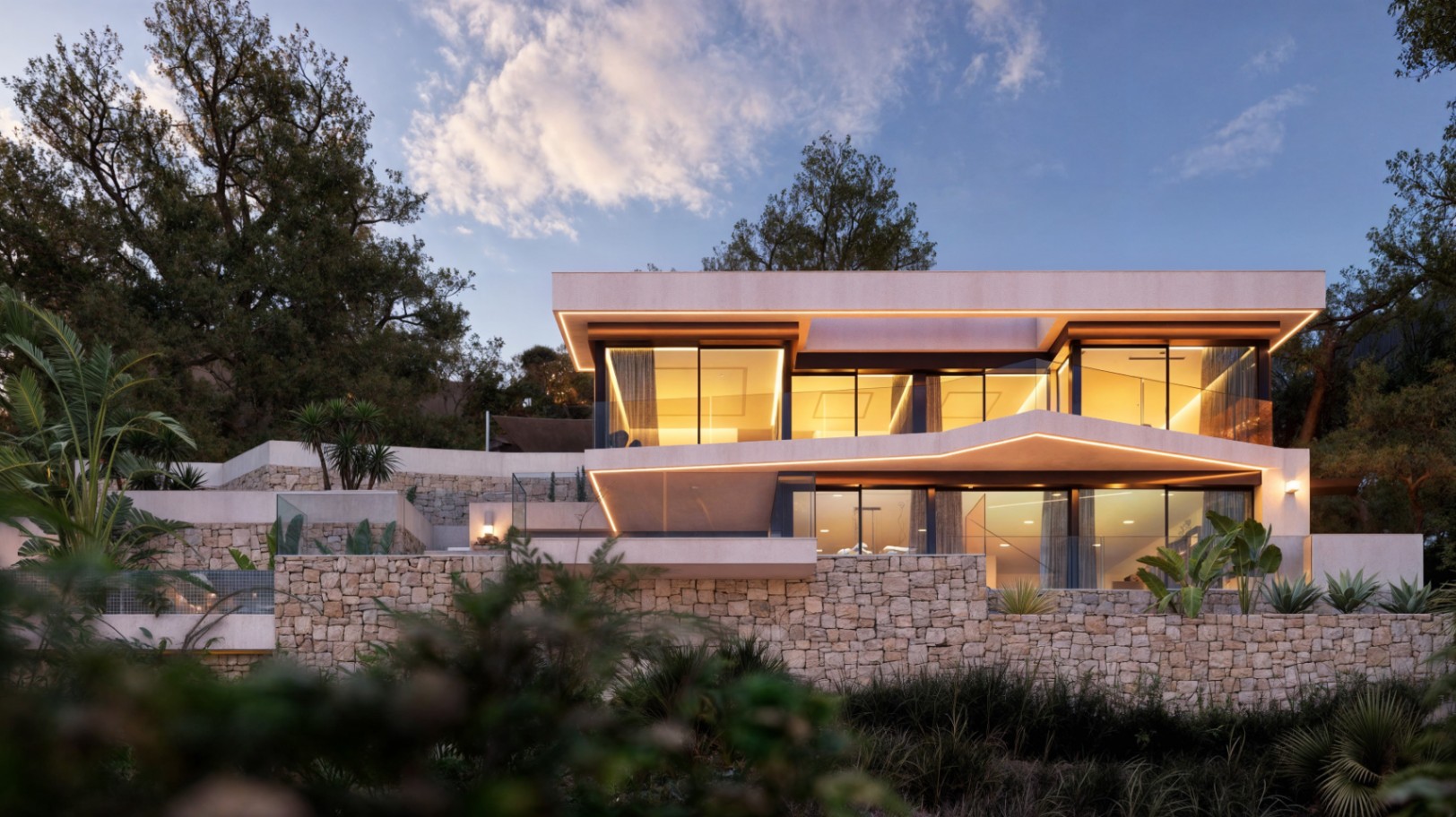 Moderne zweistöckige Fassade mit Natursteinmauern, großzügigen Glasfronten und integrierter LED-Beleuchtung, die die architektonischen Linien in der Dämmerung betont.