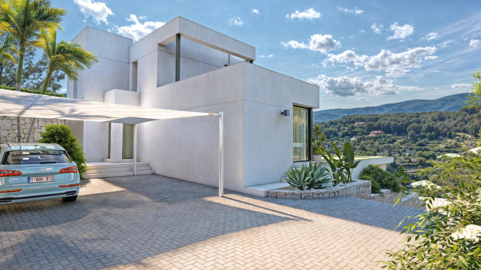 Minimalistische Villa mit gepflasterter Einfahrt, Sonnensegel und Natursteinmauern, die einen weiten Blick auf die Sierra de Bernia bieten.