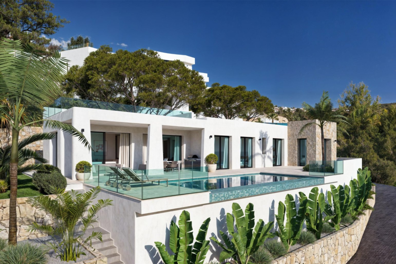 Außenansicht der Villa mit Pool, Terrasse mit Liegestühlen und mediterranem Garten mit Palmen.