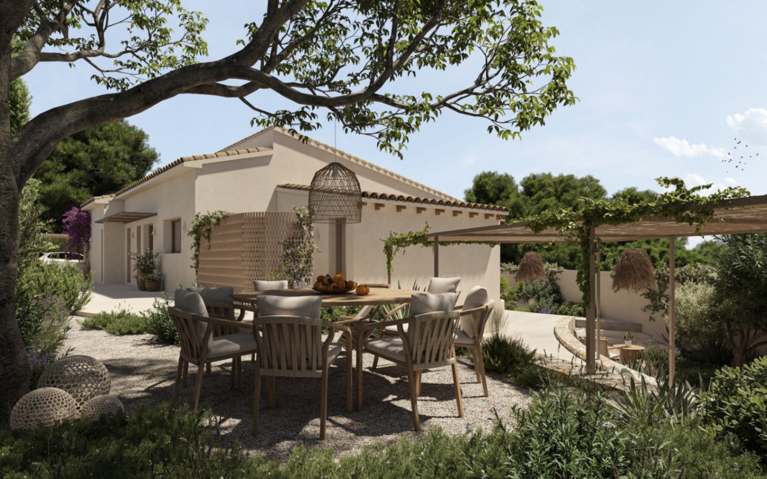 Außen-Essbereich mit rundem Holztisch auf Kies, beschattet von einem alten Baum und einer Pergola mit Kletterpflanzen vor der mediterranen Fassade der Villa.